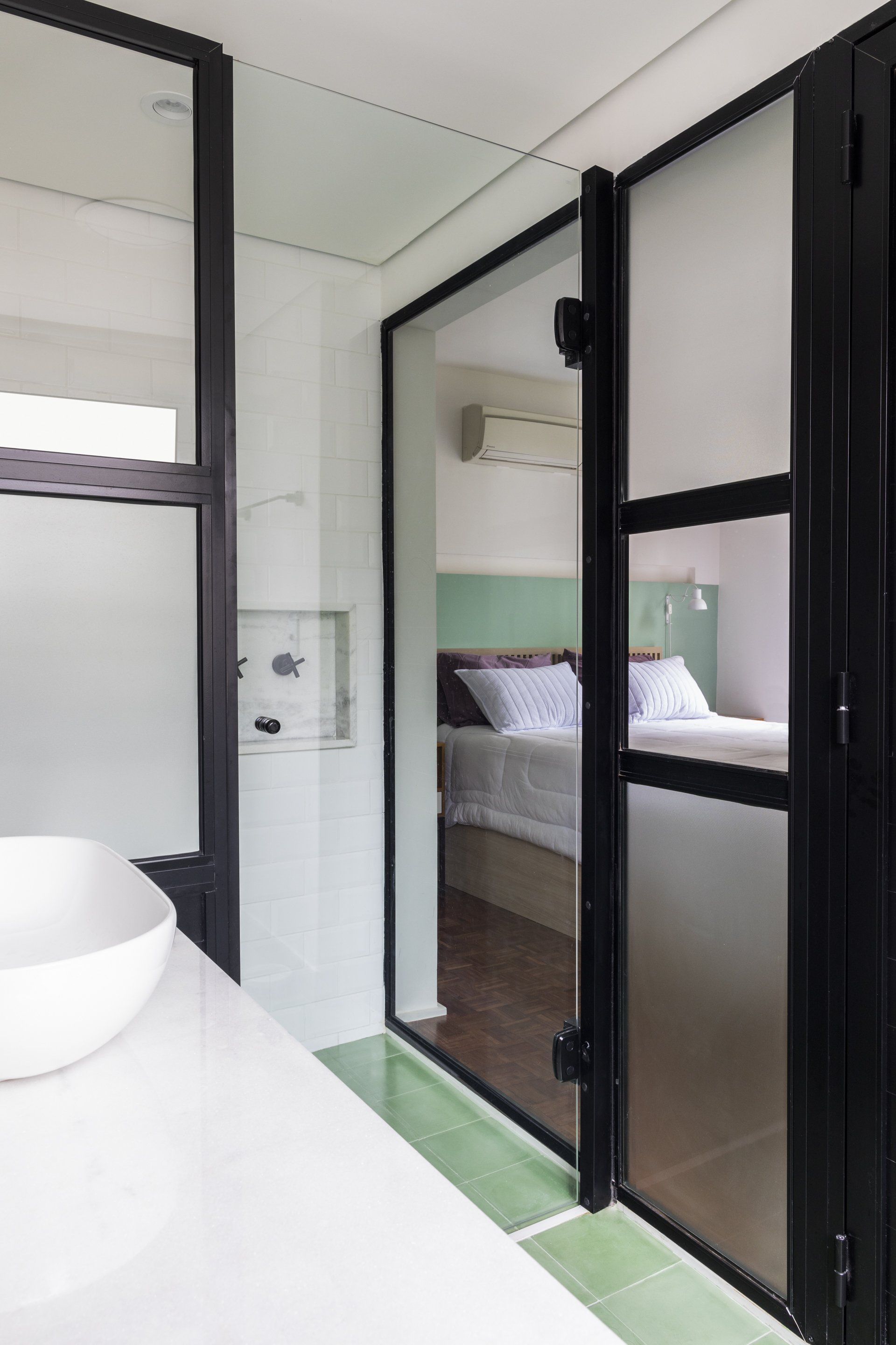 Uma casa de banho com lavatório e porta de vidro que dá acesso a um quarto.