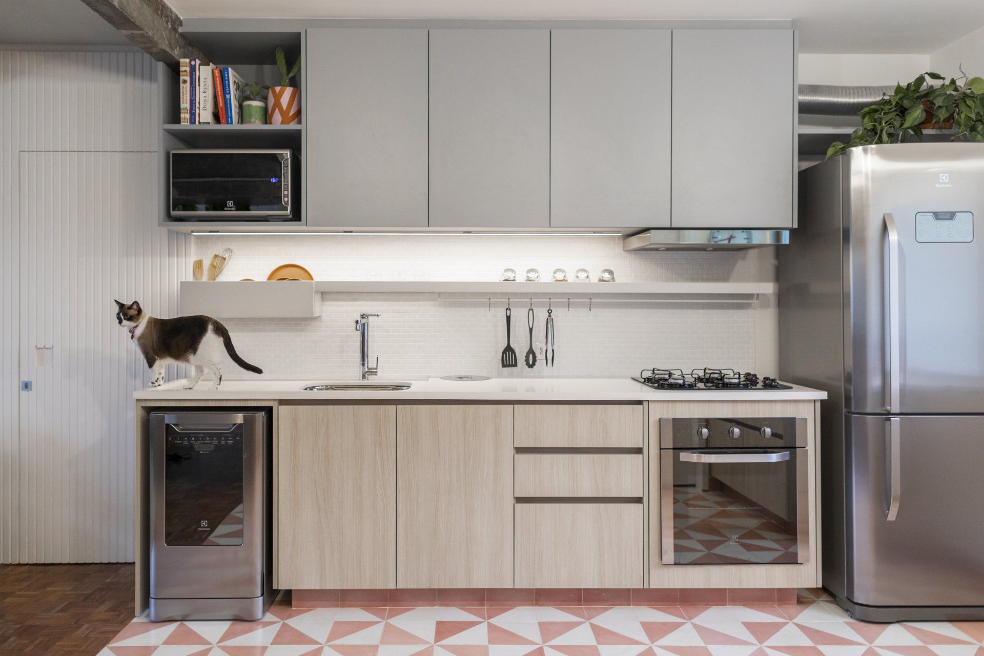 Um gato está sentado em um balcão de uma cozinha ao lado de uma geladeira.