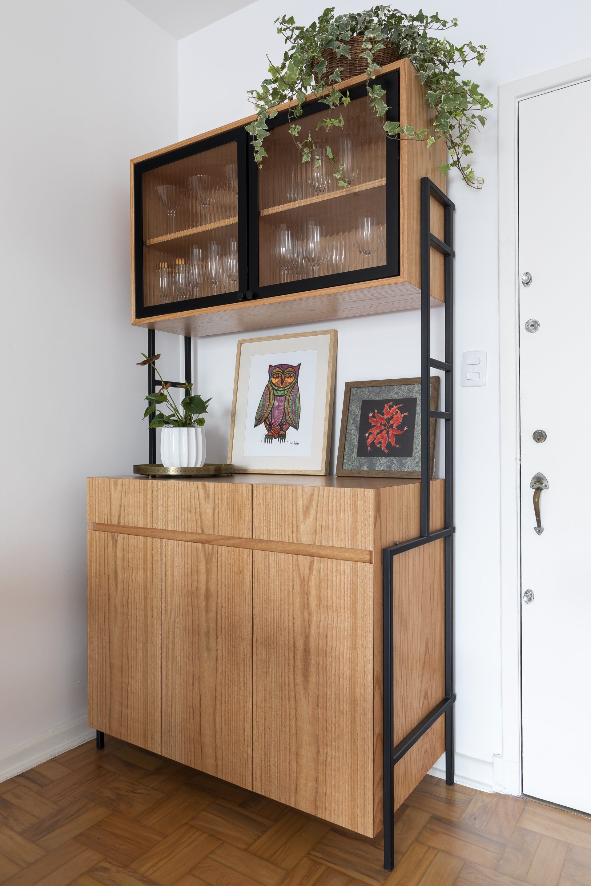 Um armário de madeira com portas de vidro fica em uma sala ao lado de uma porta.