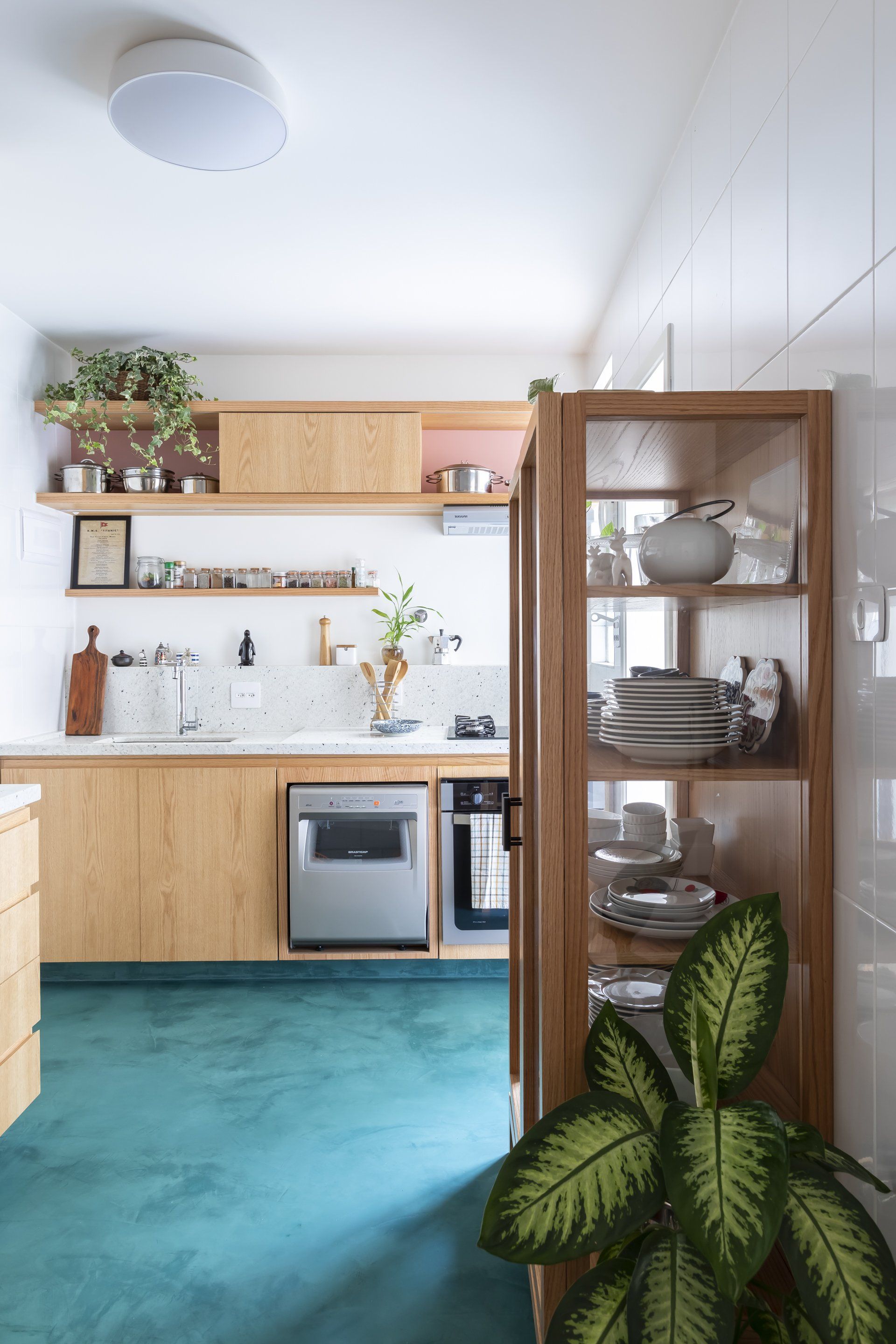 Uma cozinha com piso verde, armários de madeira e cristaleira.