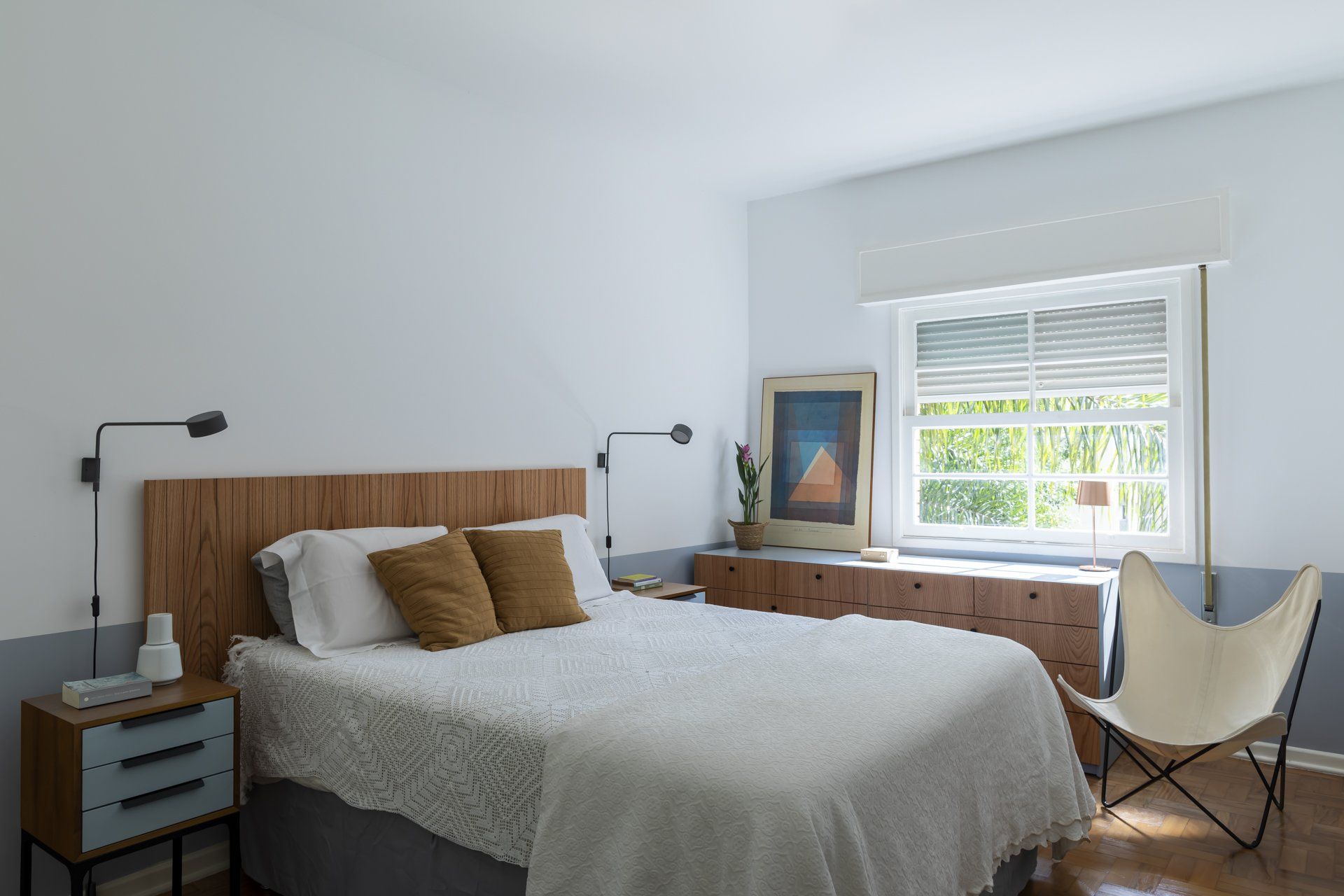 Um quarto com cama, mesa de cabeceira, cadeira e janela.