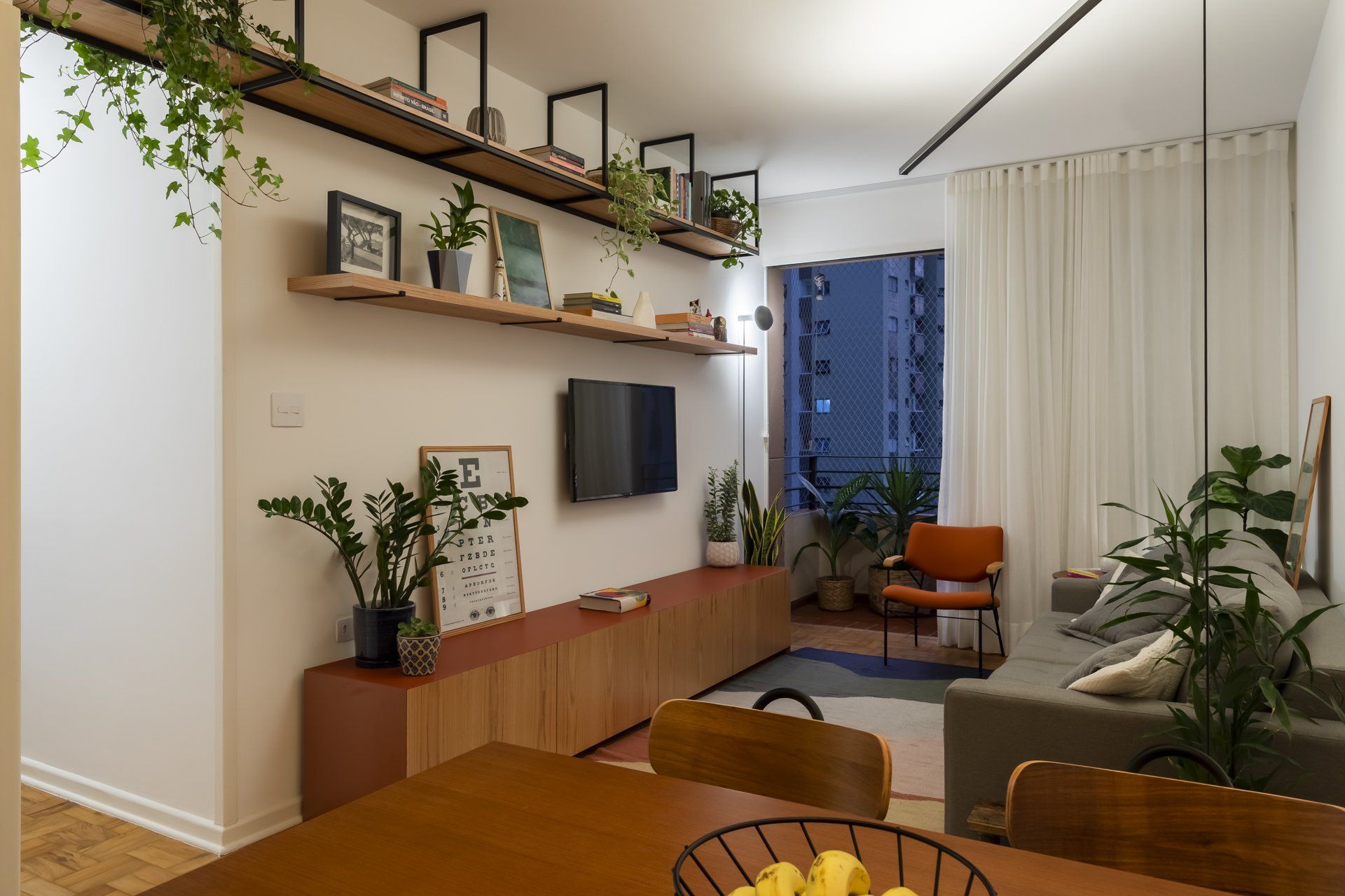 Uma sala de estar com sofá, mesa, cadeiras e TV de tela plana.