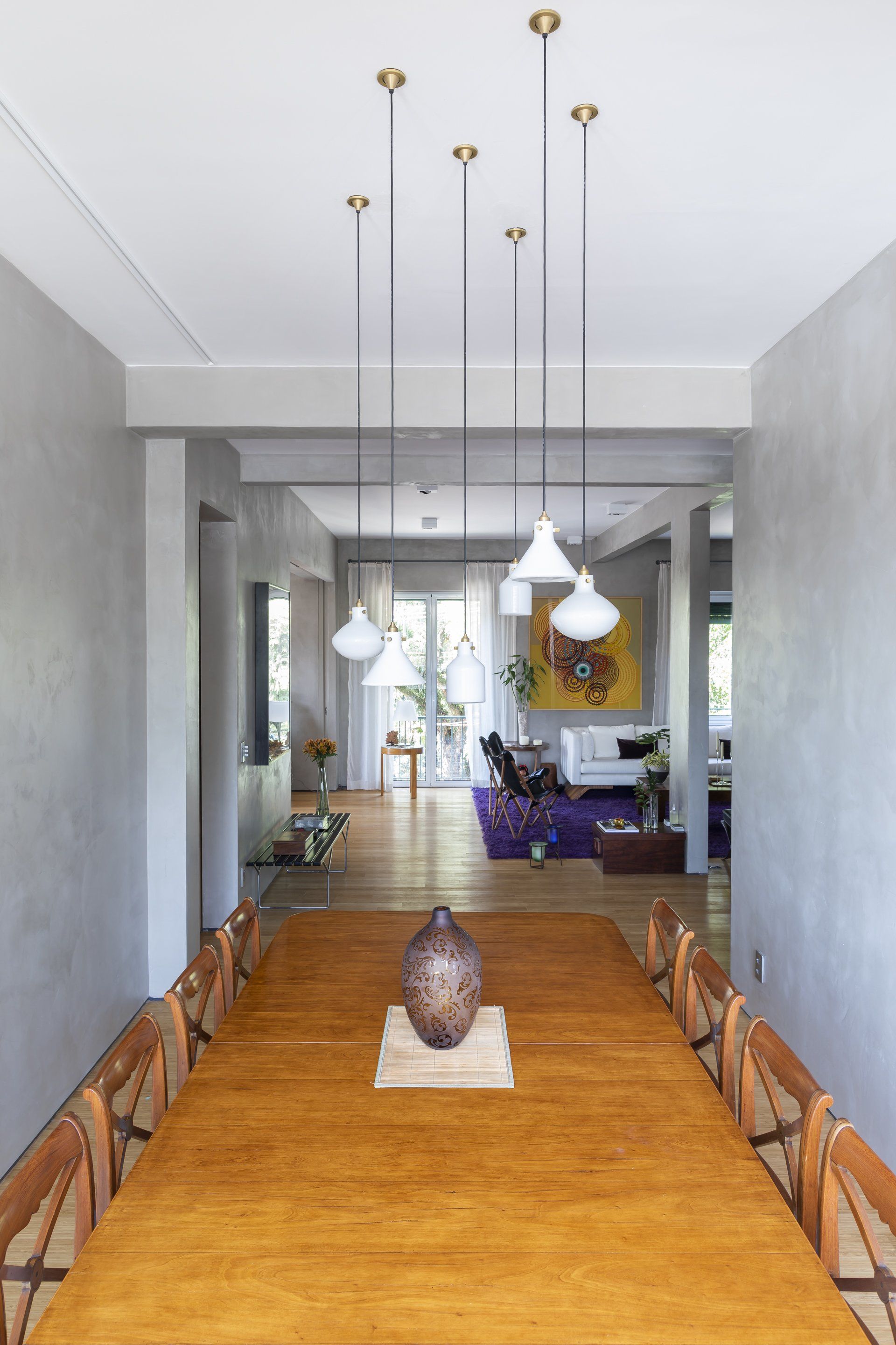 Uma longa mesa de madeira com um vaso em cima em uma sala de jantar.