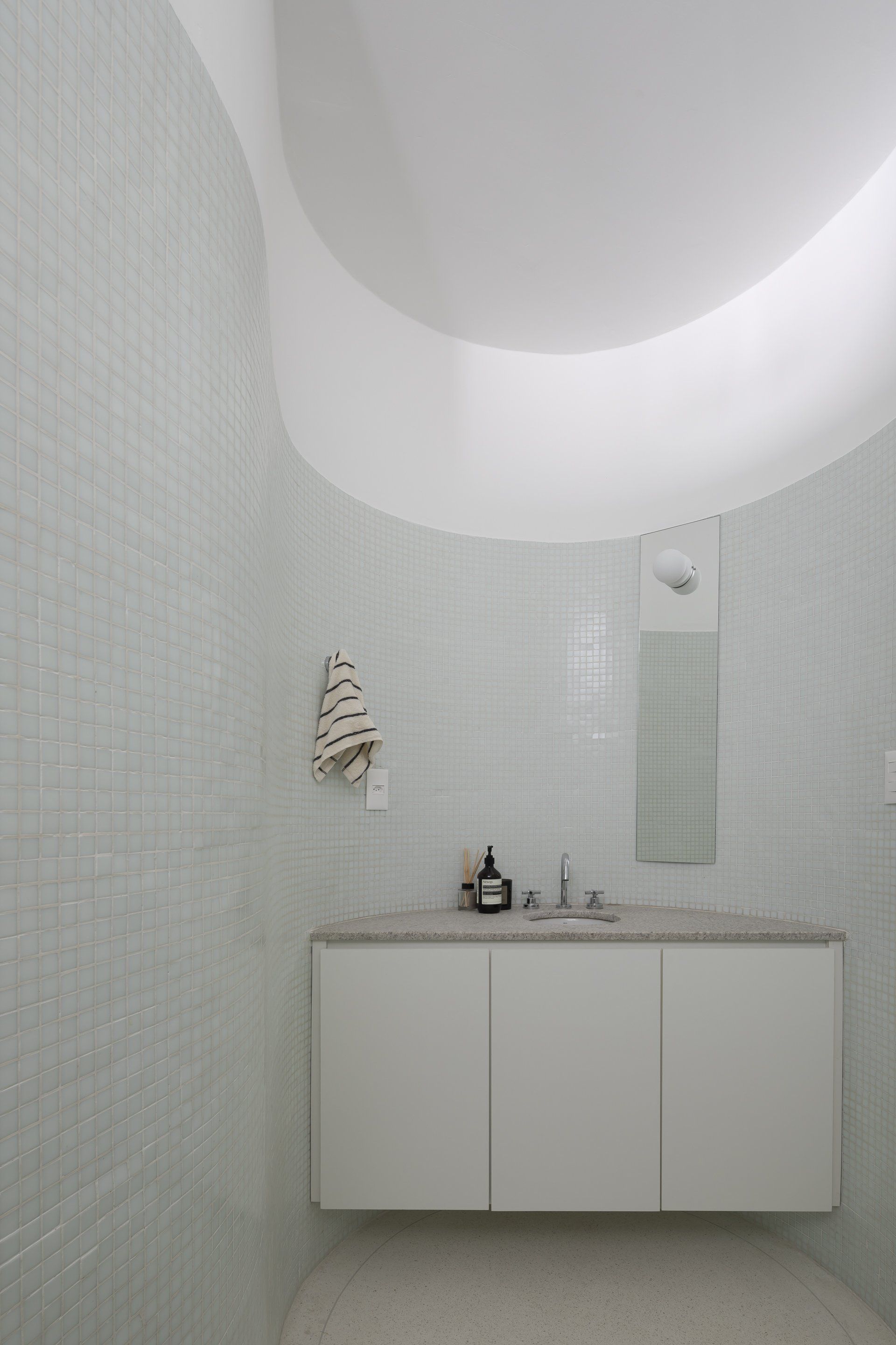 Uma casa de banho com azulejos brancos, lavatório e espelho.