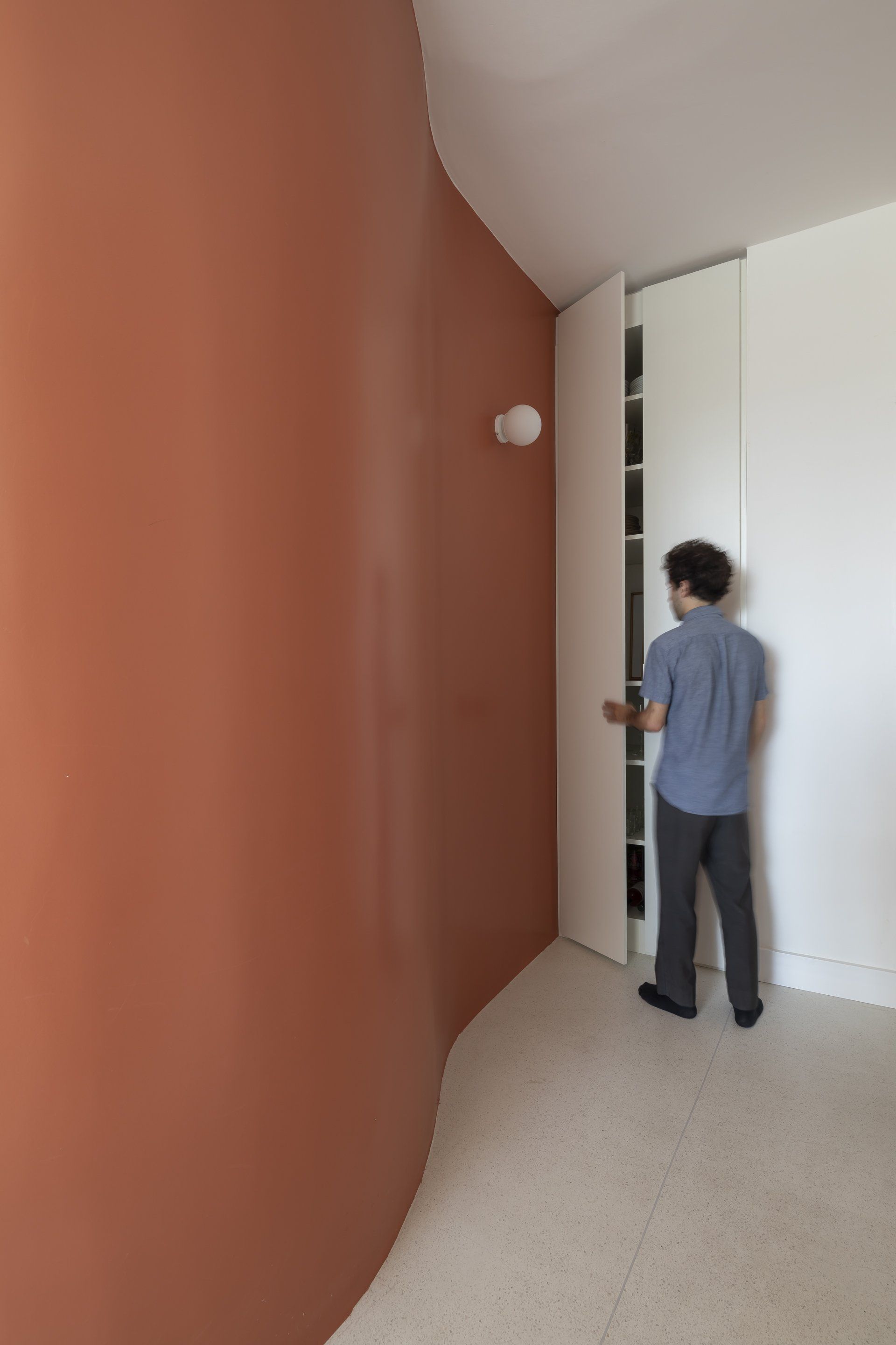 Um homem está parado em um corredor olhando dentro de um armário.