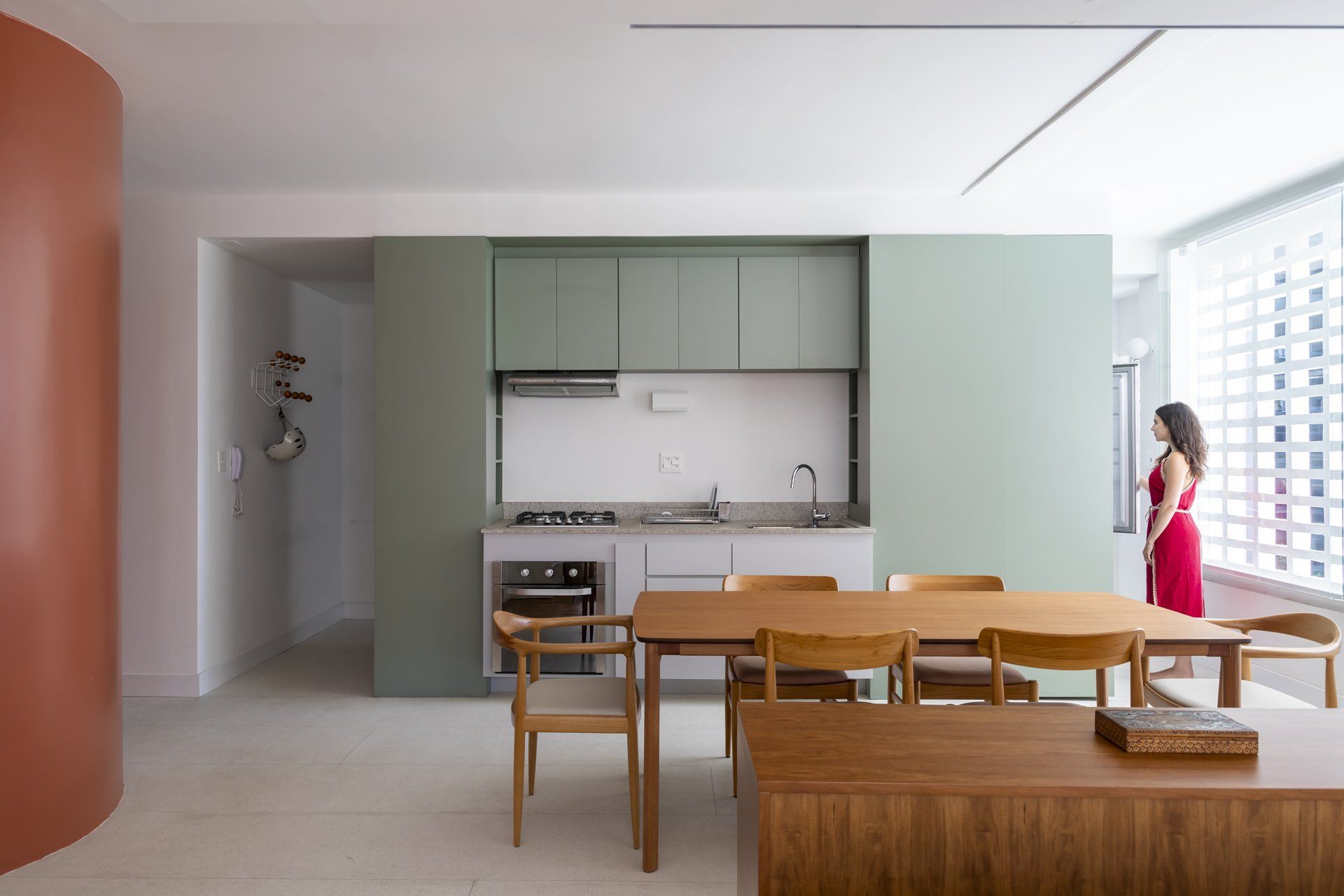 Uma mulher com um vestido vermelho está em uma cozinha ao lado de uma mesa e cadeiras.