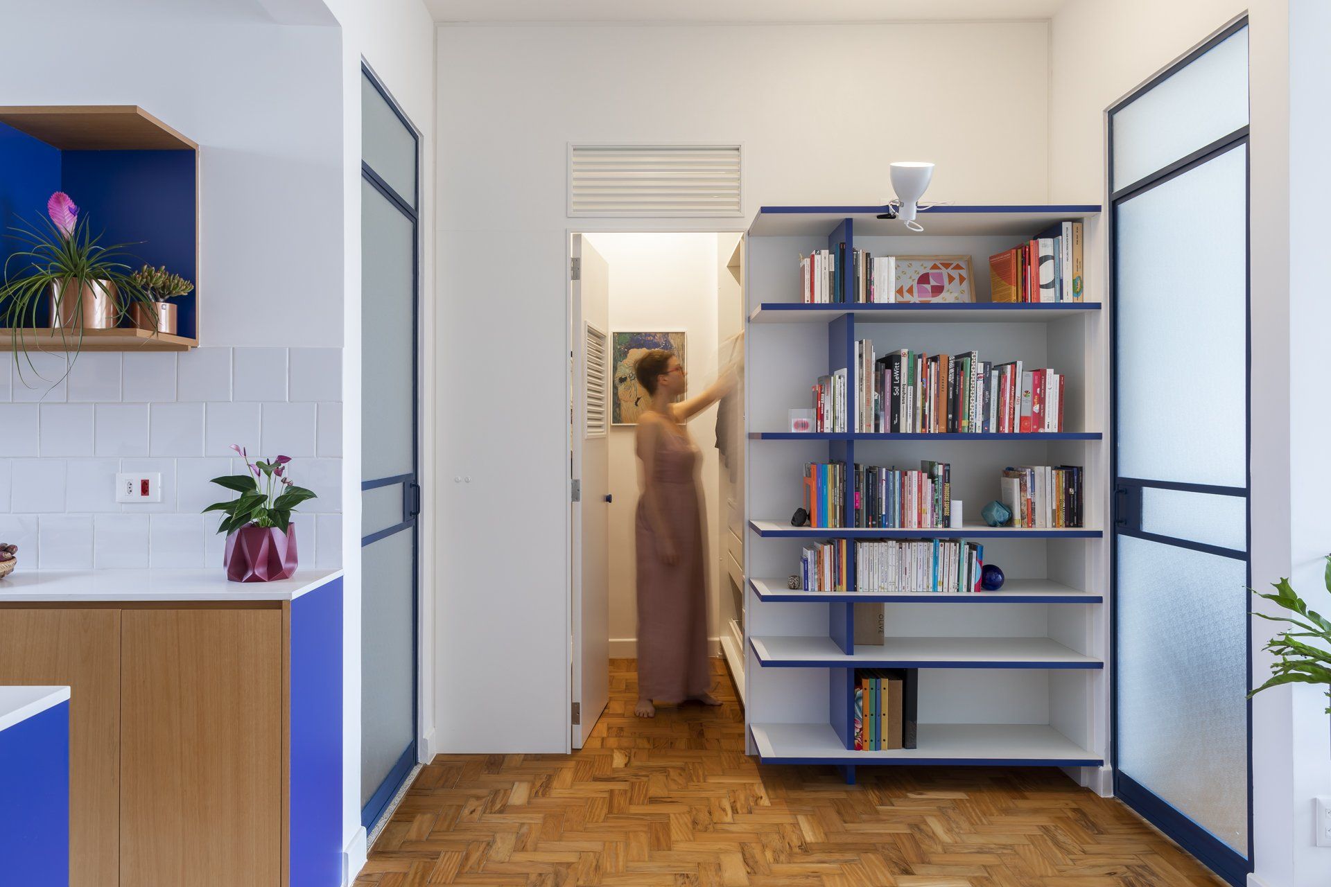 Uma mulher está parada ao lado de uma estante de livros em uma sala.