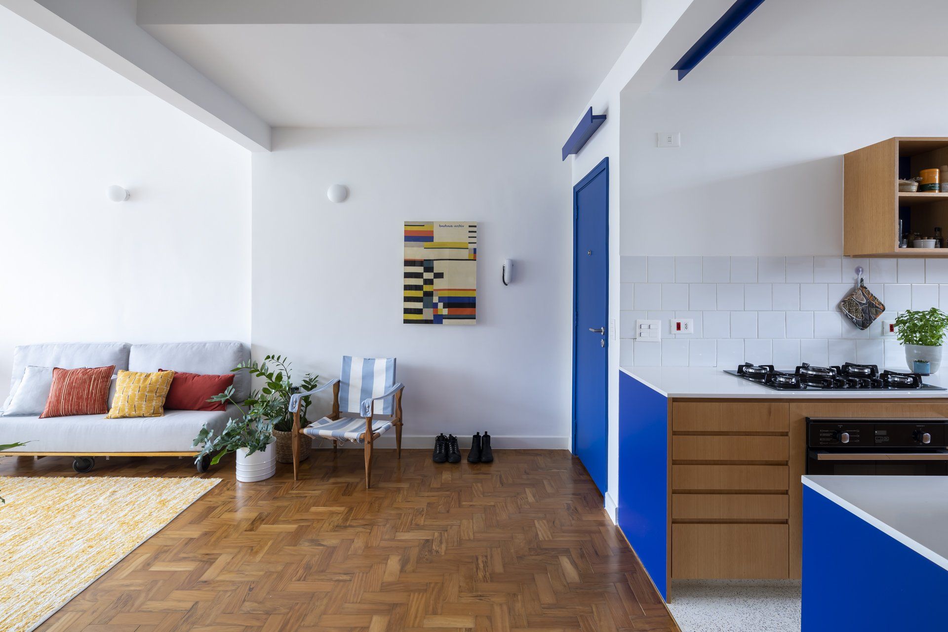 Uma sala com sofá, cadeira e uma cozinha com armários azuis.