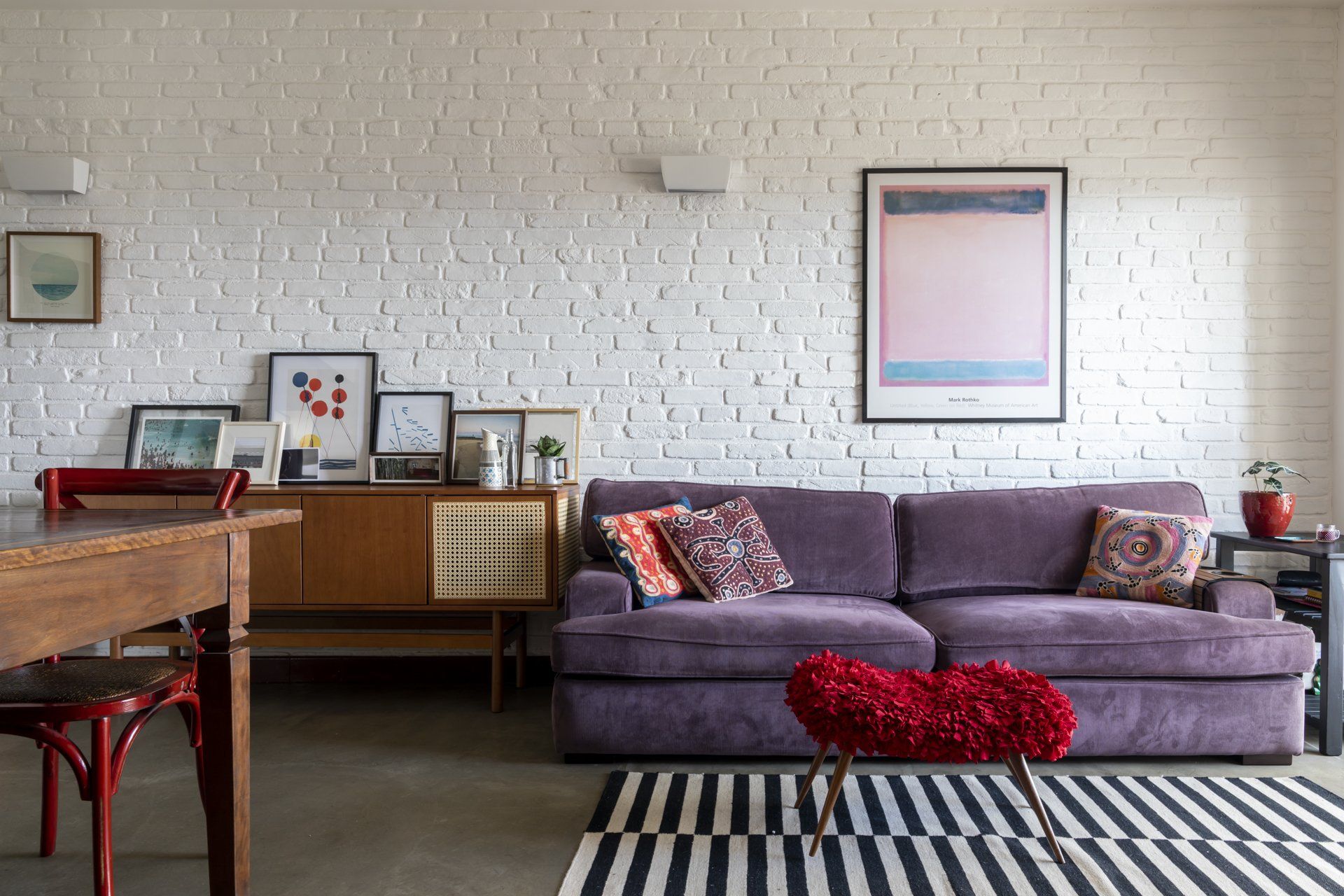Uma sala de estar com um sofá roxo e uma parede de tijolos brancos