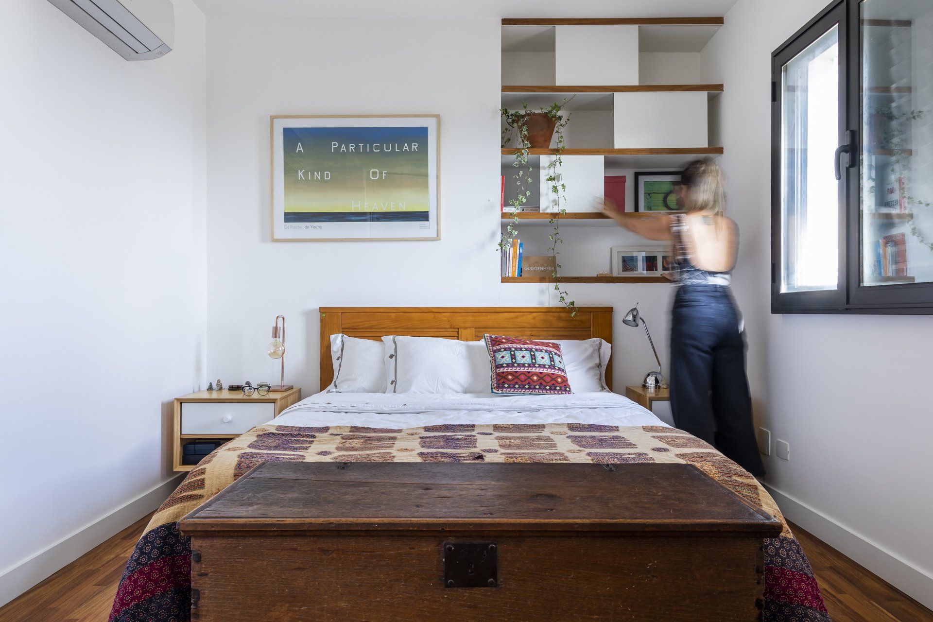 Uma mulher está ao lado de uma cama em um quarto.