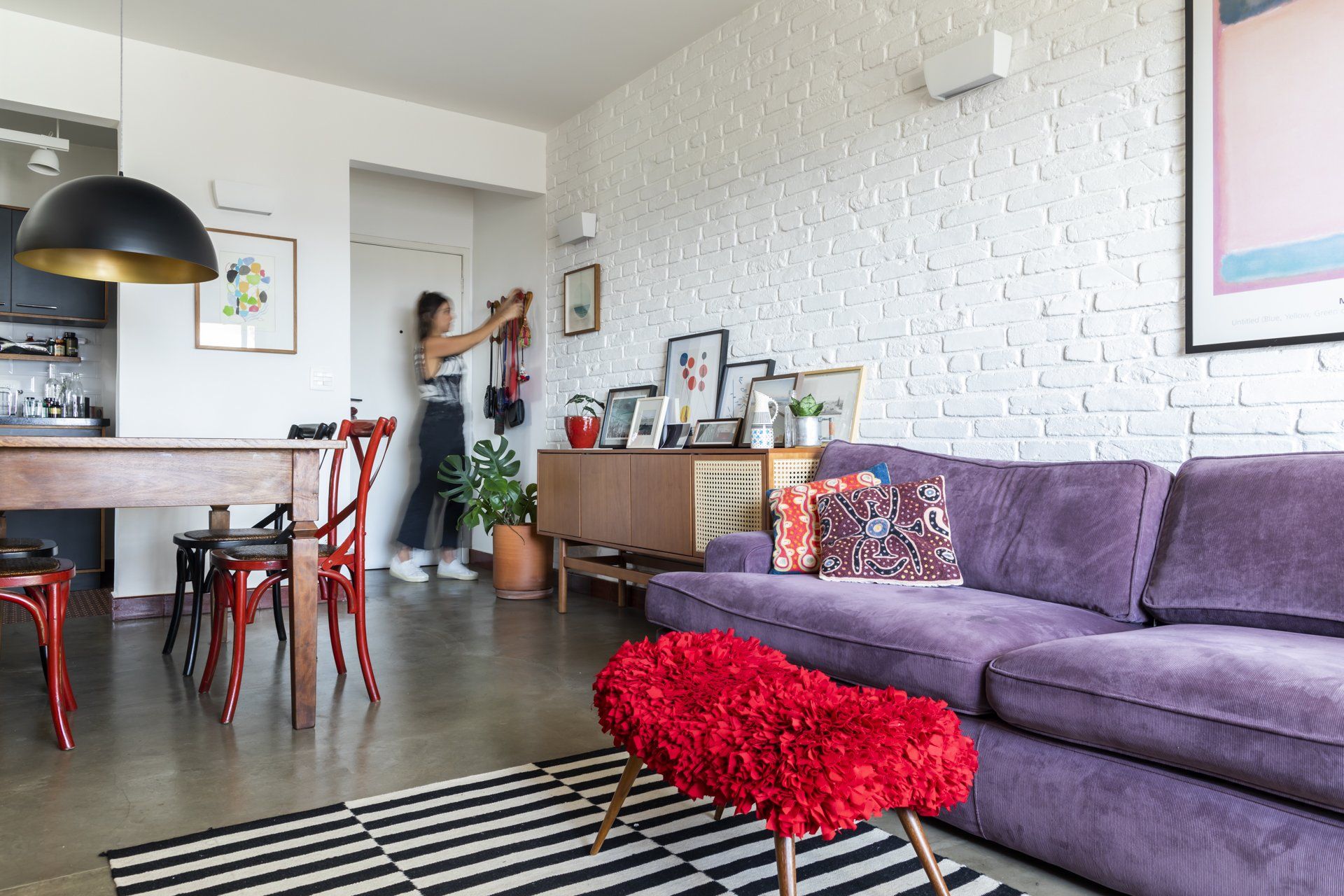 Uma mulher está em uma sala de estar com um sofá roxo e uma poltrona vermelha.
