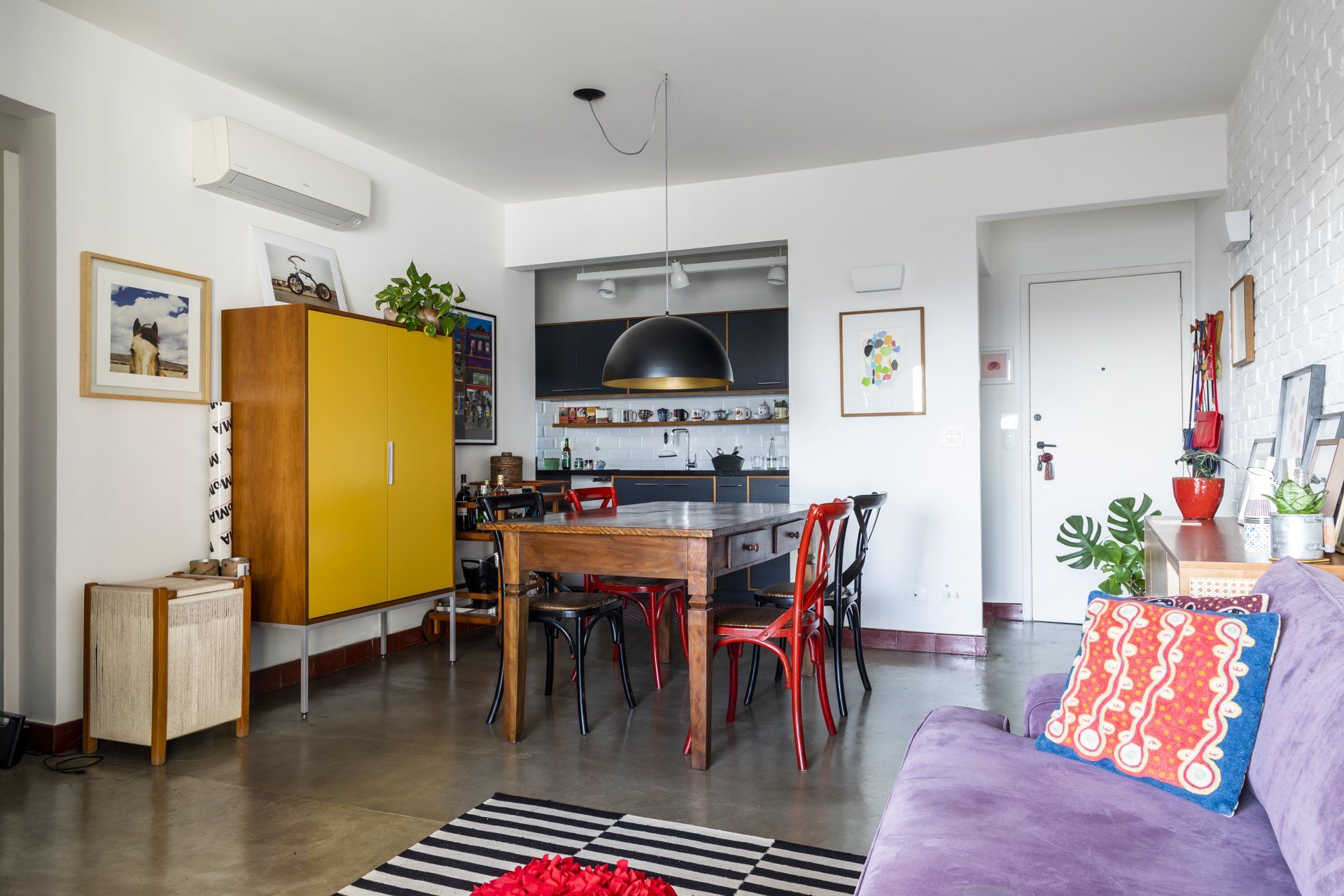 Uma sala de estar com sofá roxo, mesa e cadeiras de madeira.