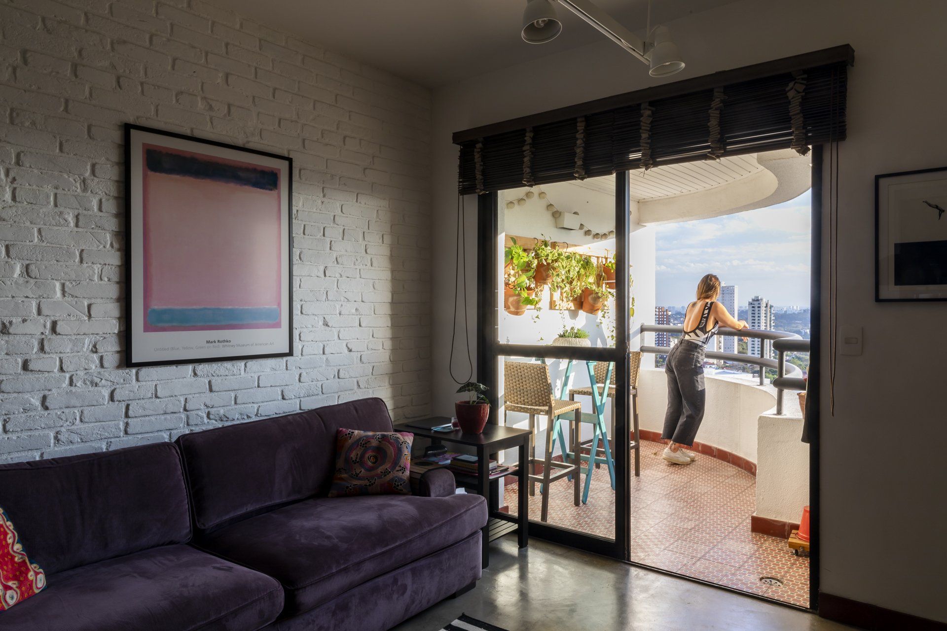 Uma sala de estar com um sofá roxo e uma mulher em pé na varanda.