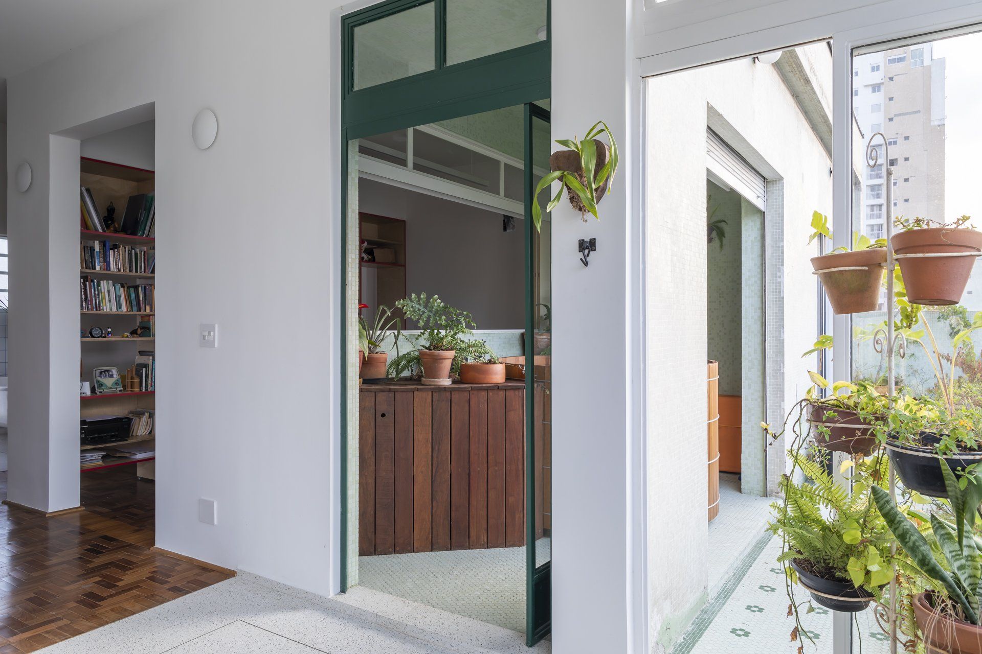 Uma sala com porta de correr de vidro que dá acesso a uma varanda repleta de vasos de plantas.