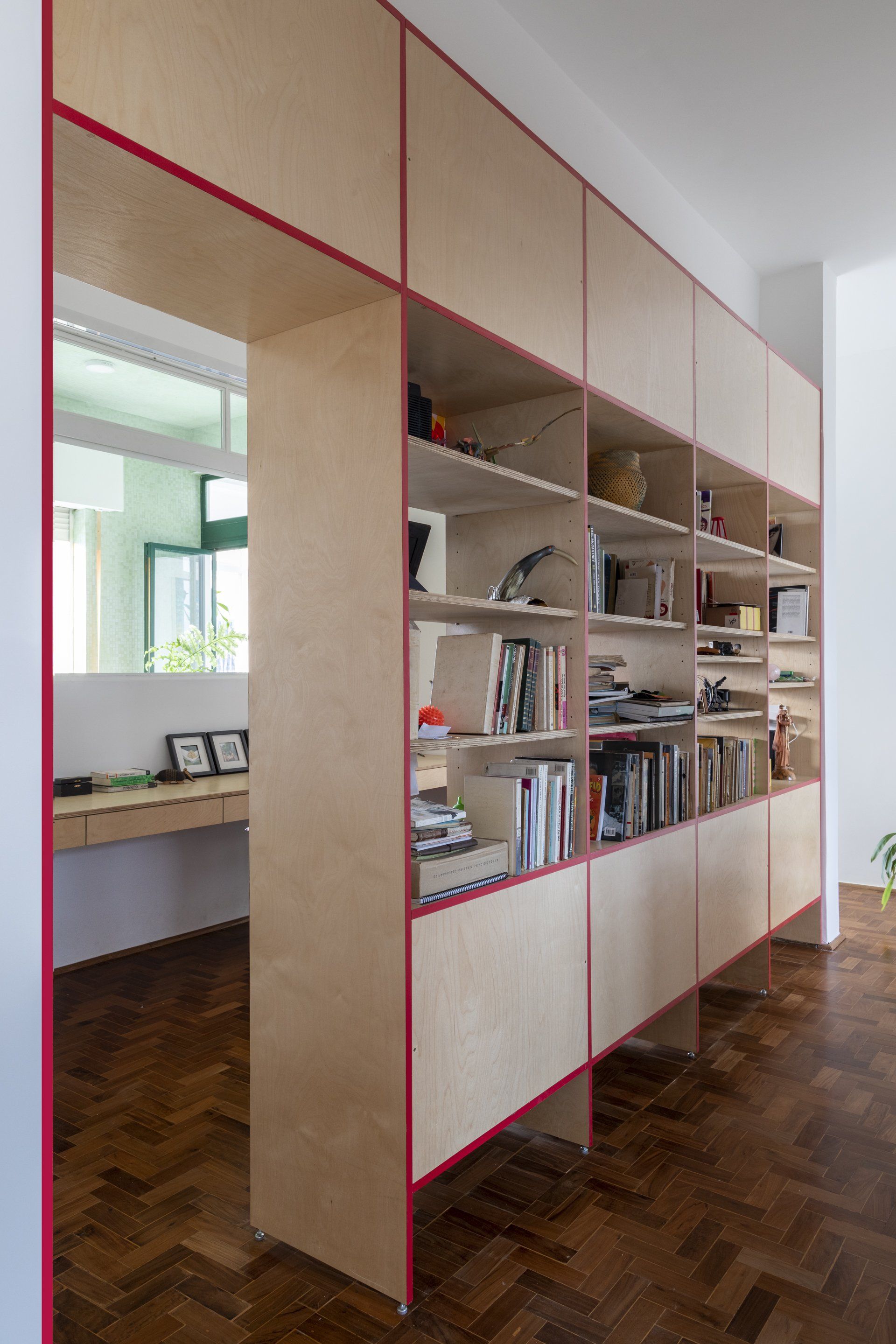 Uma estante com acabamento vermelho fica em uma sala com piso de madeira.