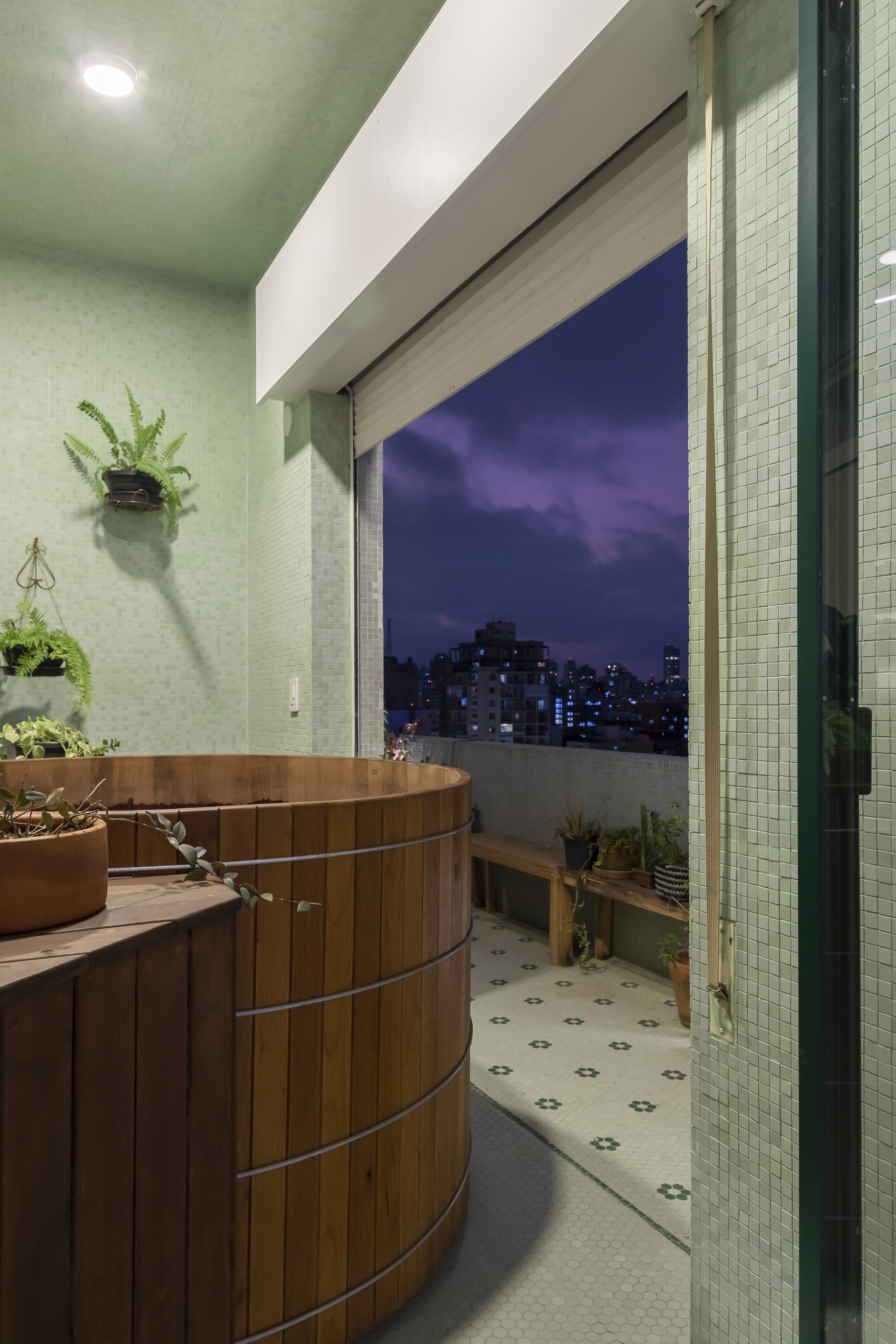 Uma banheira de madeira está em uma varanda ao lado de uma janela.