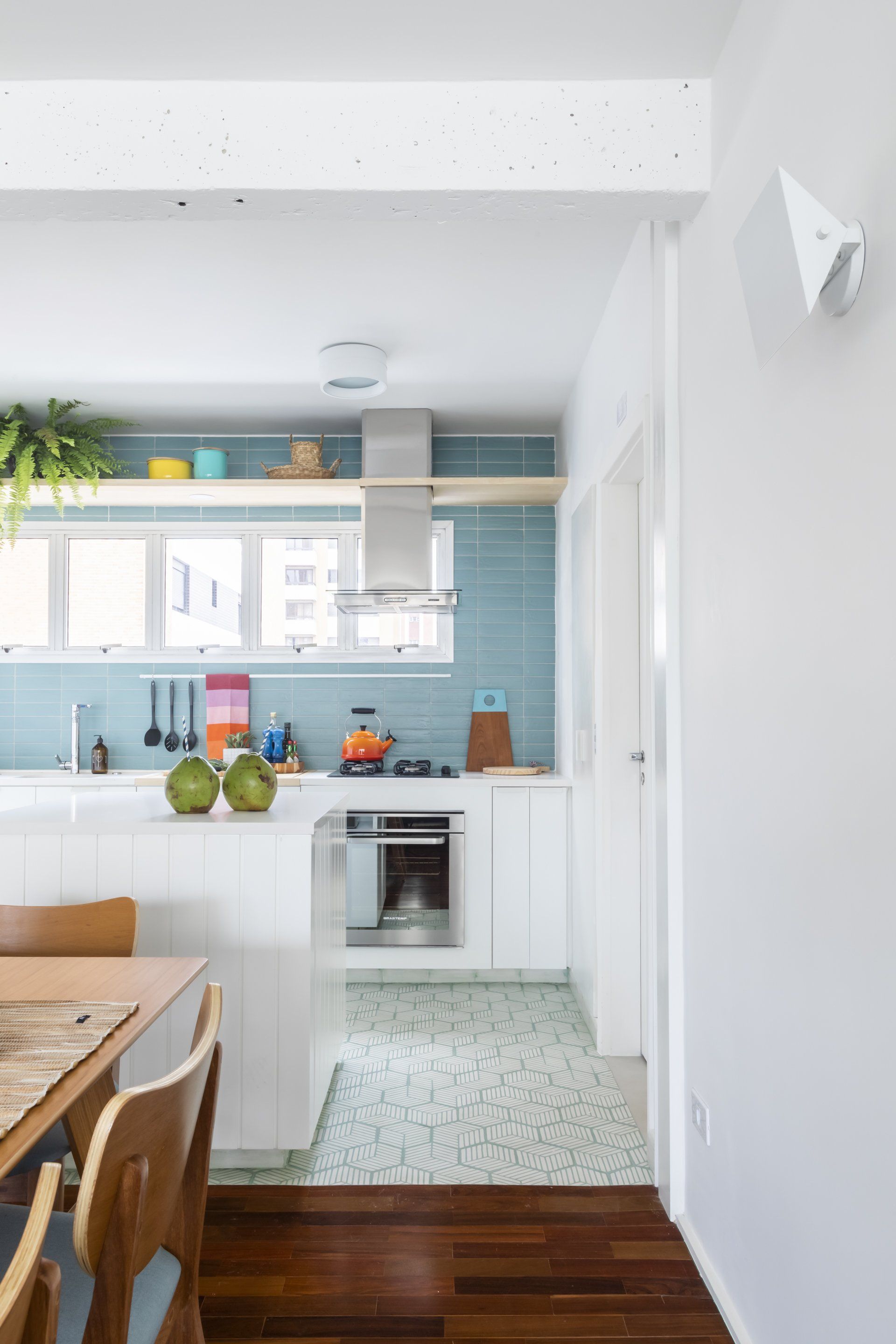 Uma cozinha com armários brancos e azulejos azuis está ligada a uma sala de jantar.