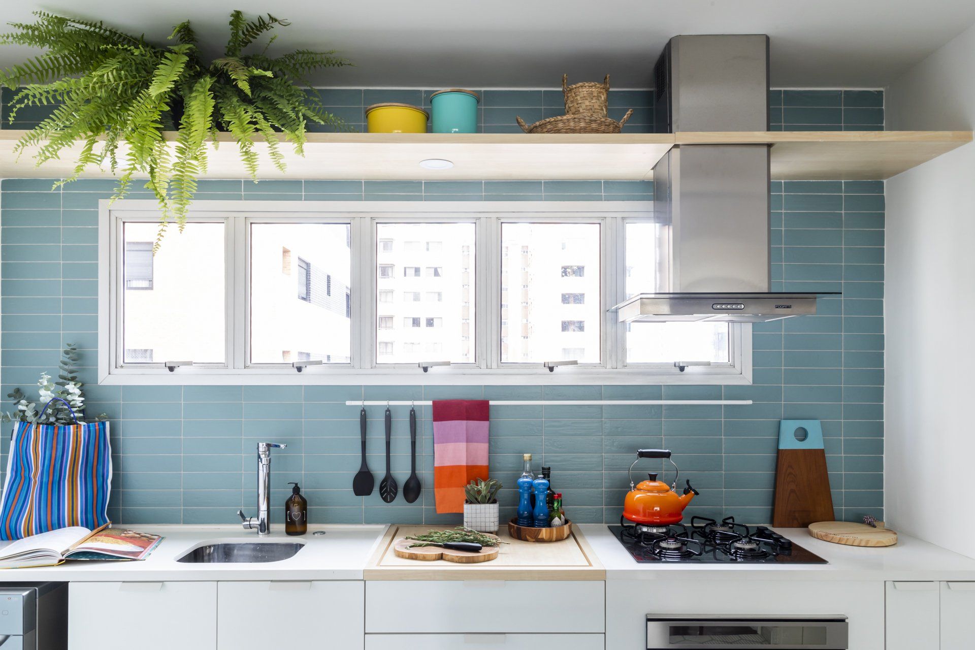 Uma cozinha com azulejos azuis, armários brancos, fogão, pia e janela.