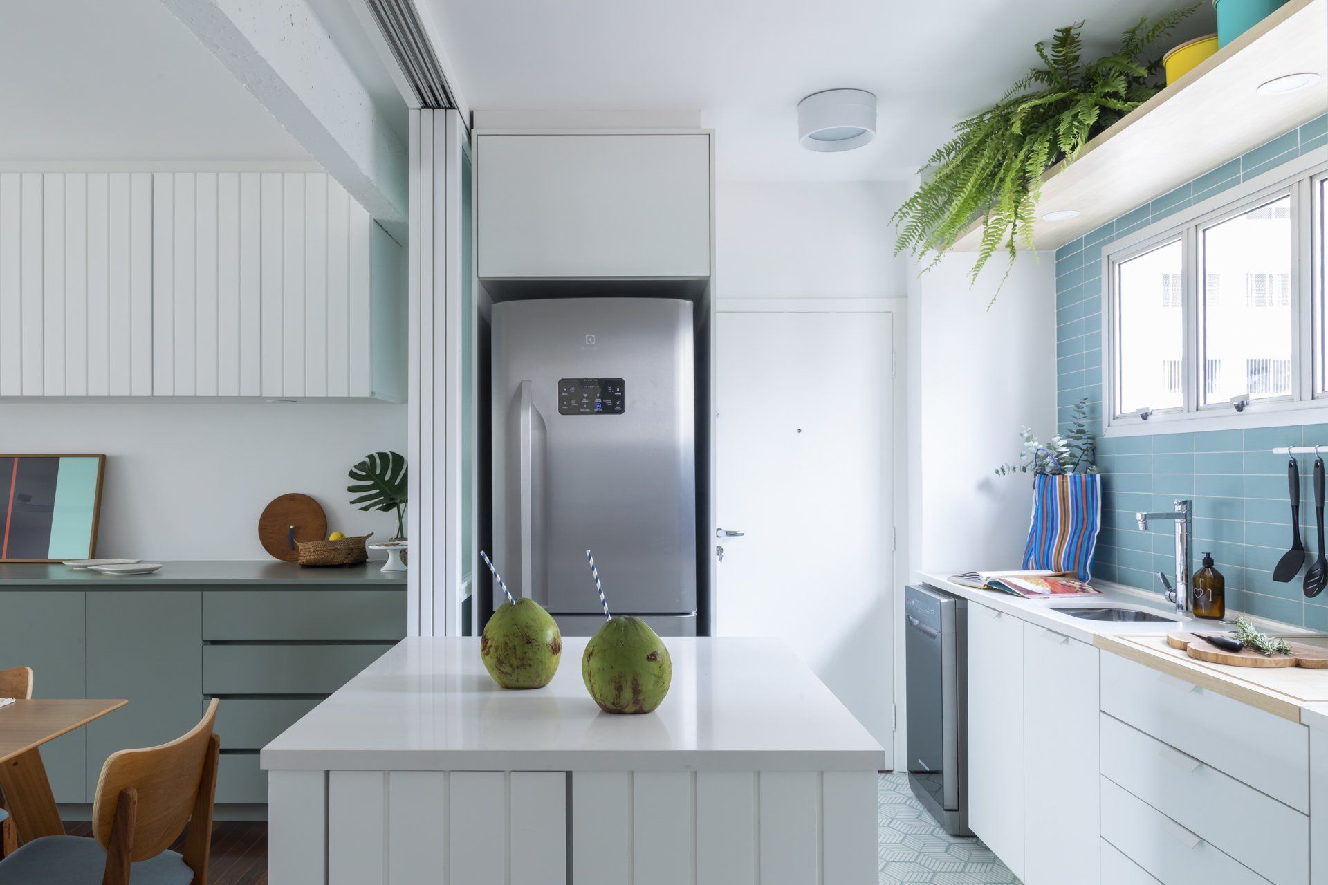 Uma cozinha com armários brancos, geladeira, pia e mesa.