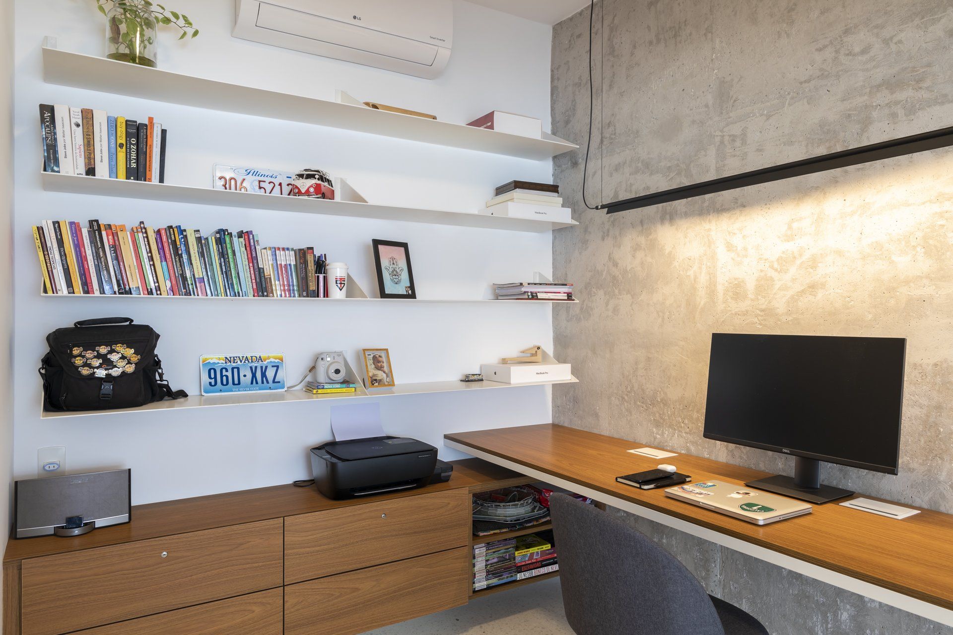 Um home office com mesa, computador, impressora e estantes repletas de livros.