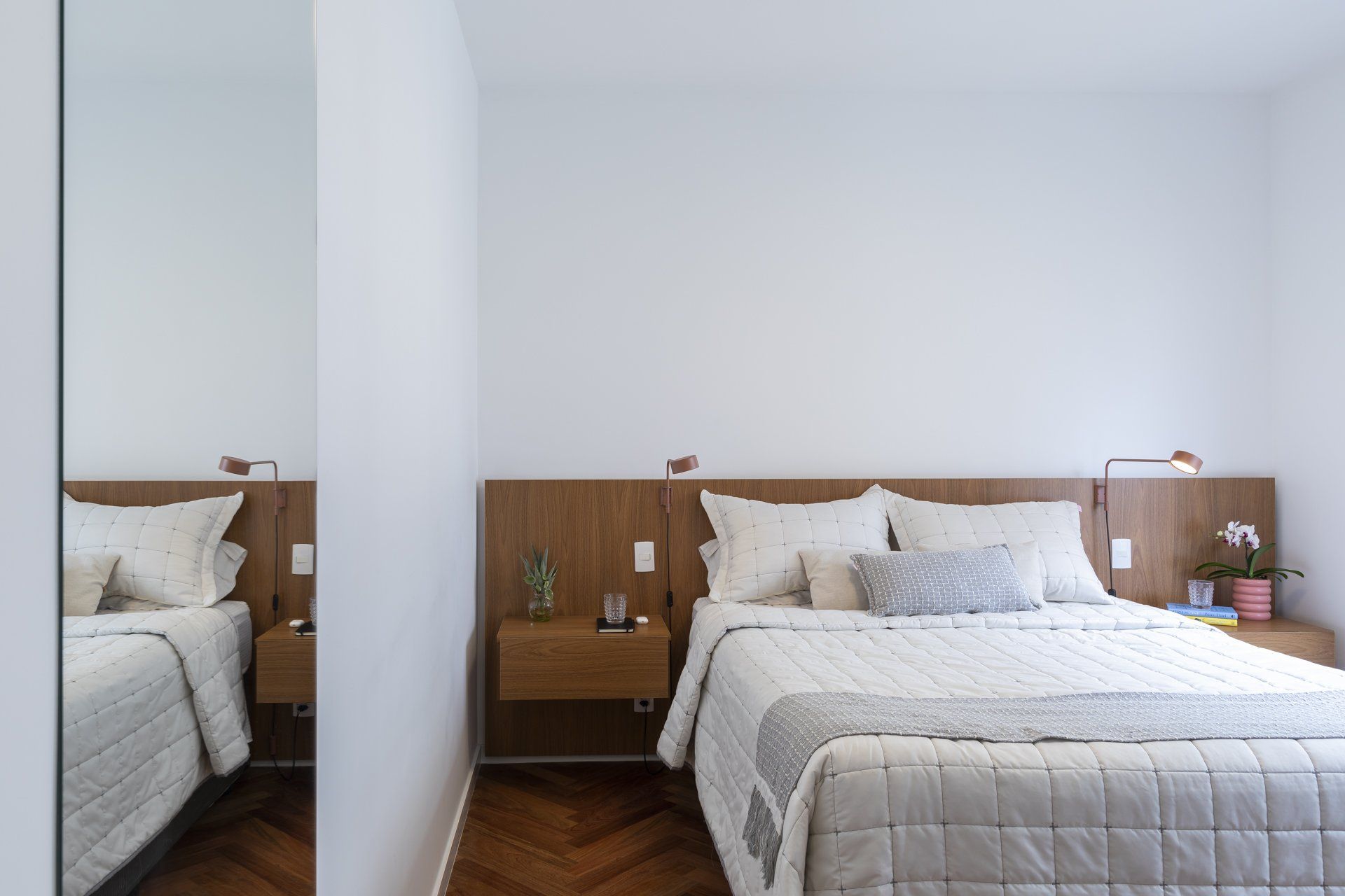 Um quarto com cama, mesinhas de cabeceira e espelho.