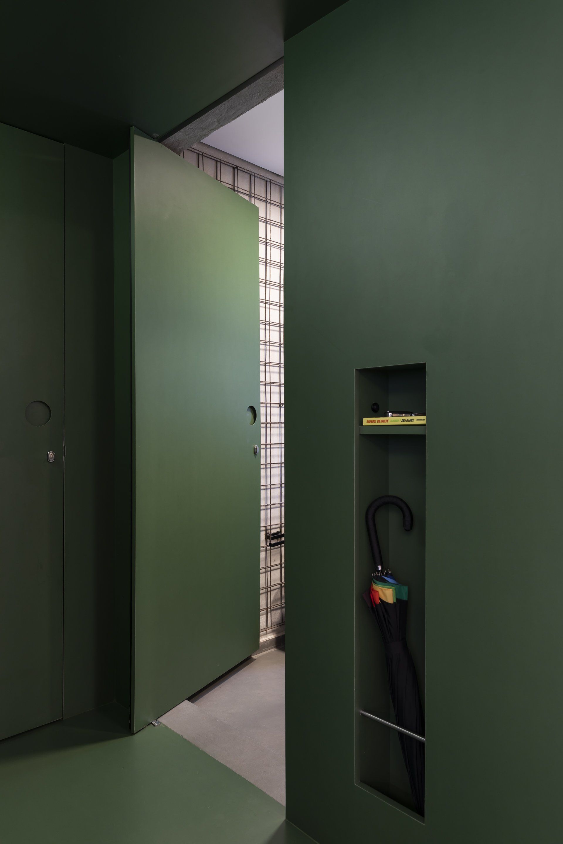Um corredor com uma porta verde e uma prateleira com um guarda-chuva.