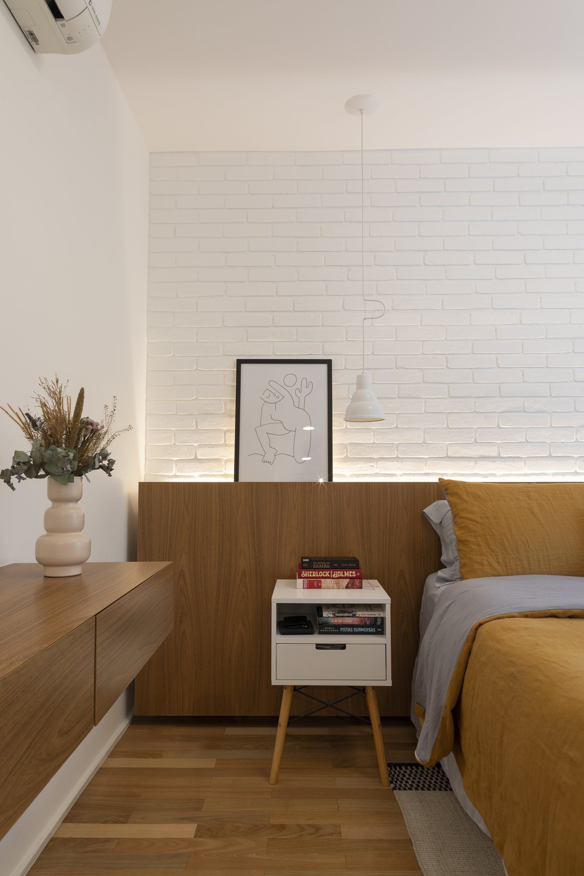 Um quarto com cama, mesa de cabeceira e parede de tijolos.