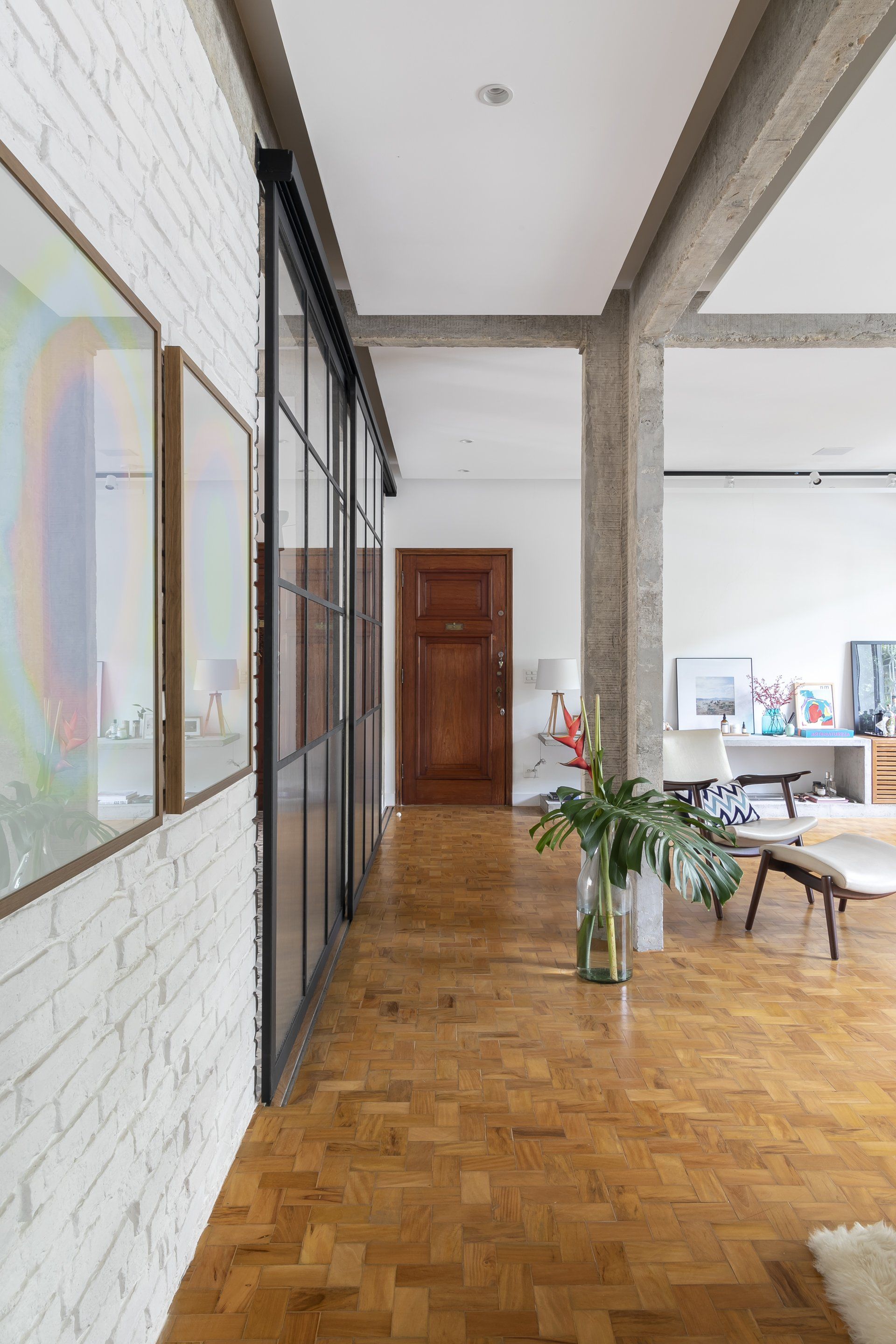 Um corredor que dá acesso a uma sala com piso de madeira e paredes de tijolos brancos.