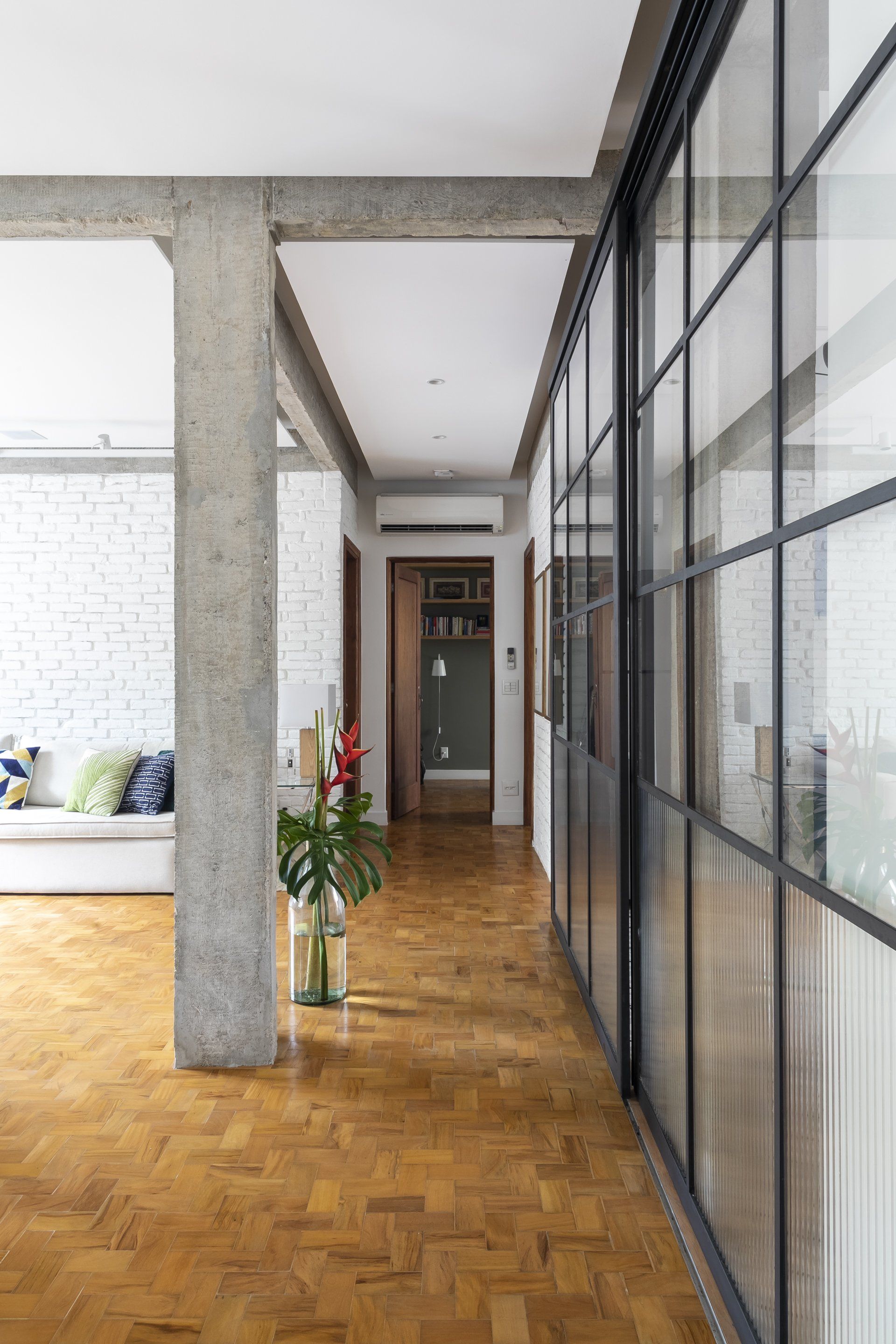 Um longo corredor com portas de vidro que dão acesso a uma sala de estar.