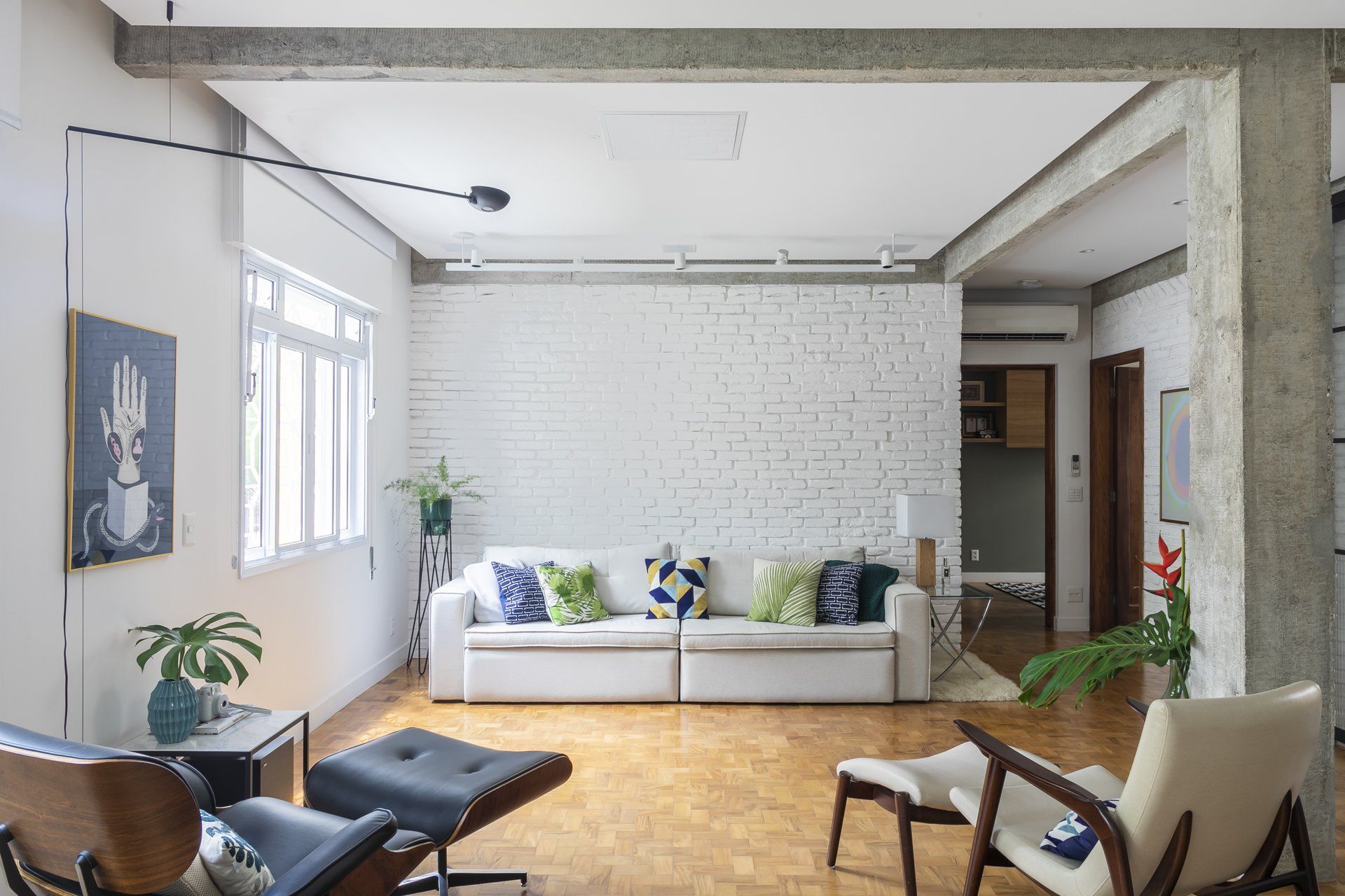 Uma sala com sofá, cadeiras, pufe e uma pintura na parede.