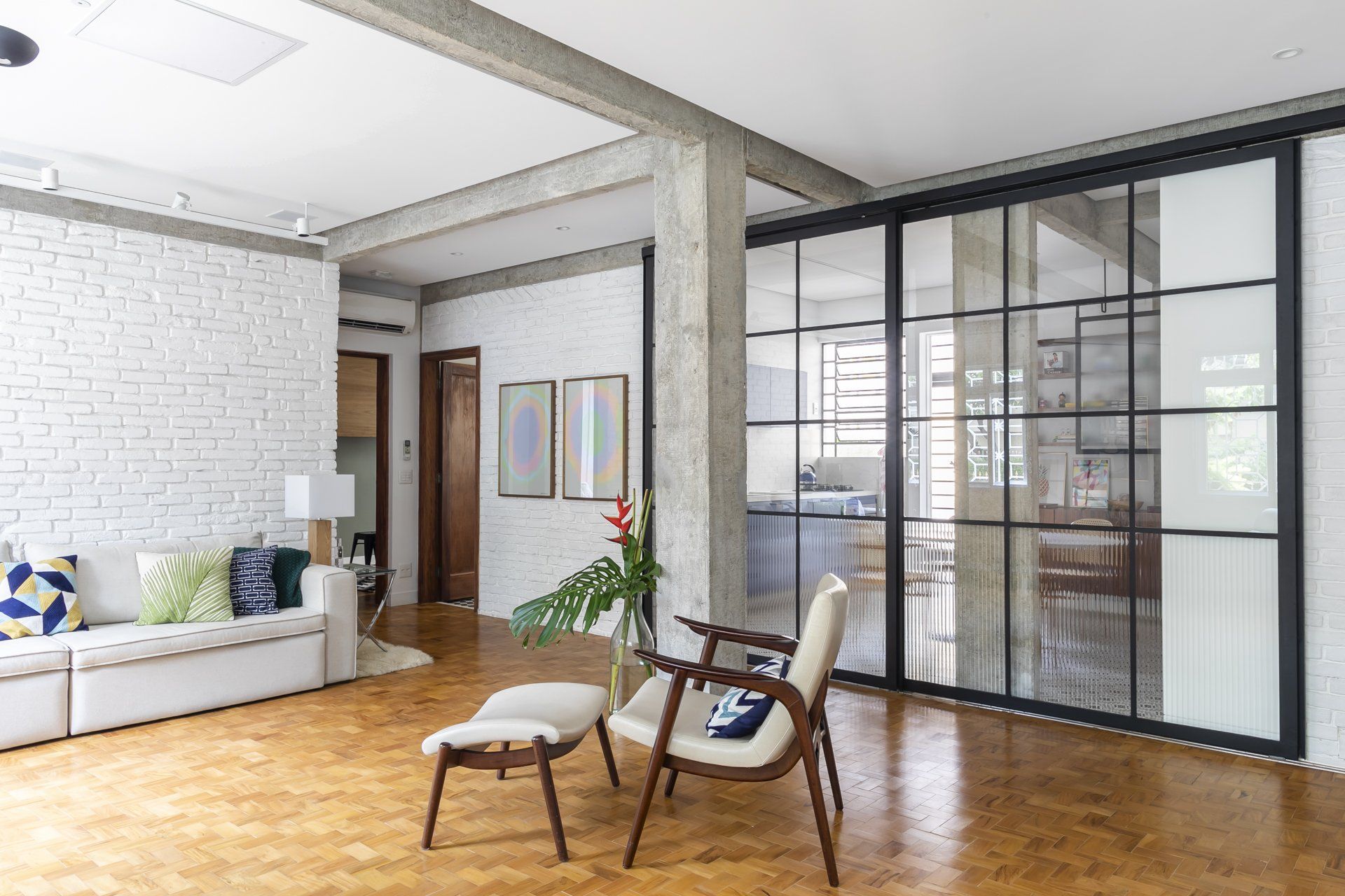 Uma sala de estar com sofá, cadeiras, pufe e portas de correr de vidro.