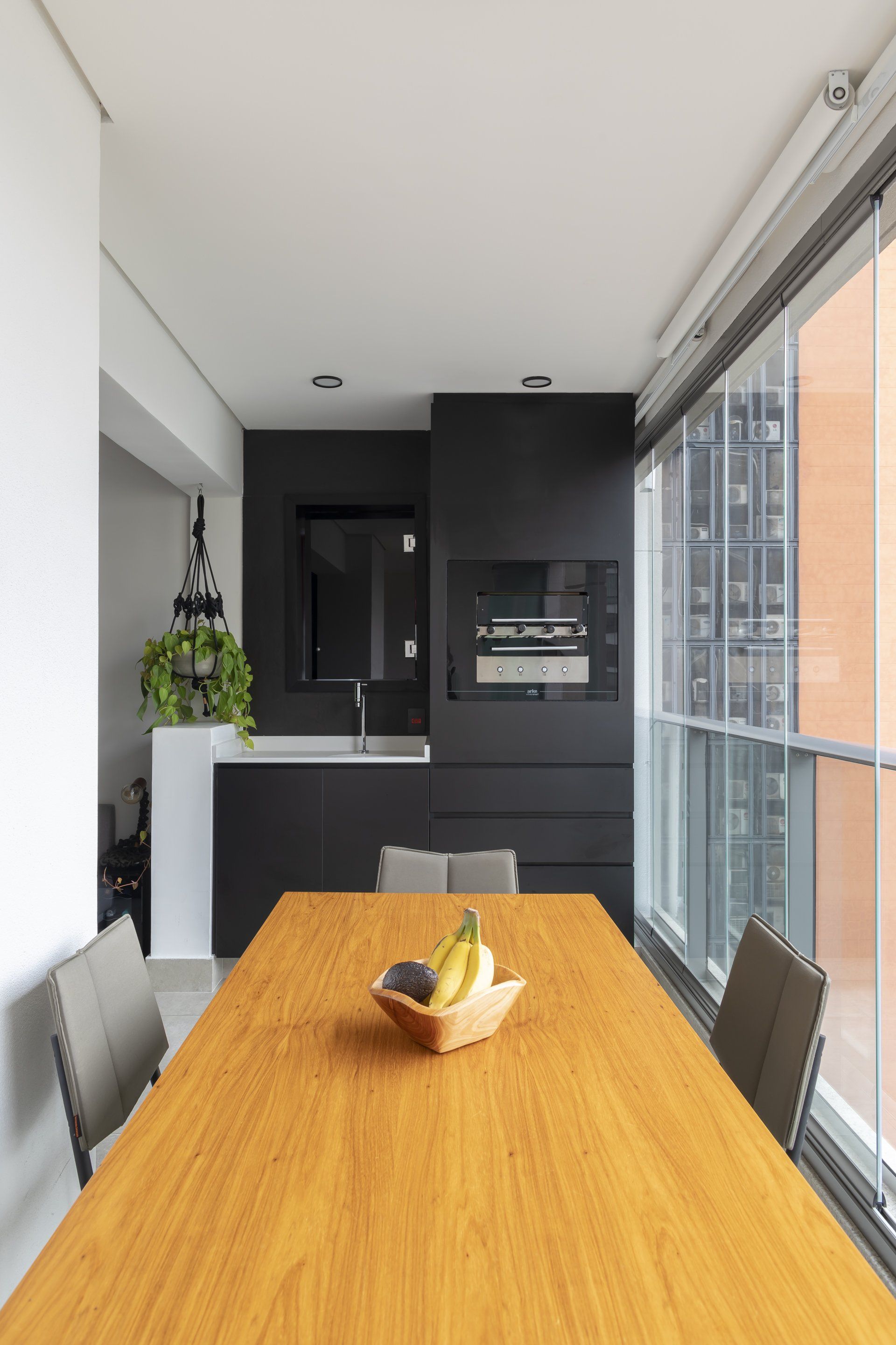 Uma mesa de madeira com uma tigela de frutas em uma sala com muitas janelas.