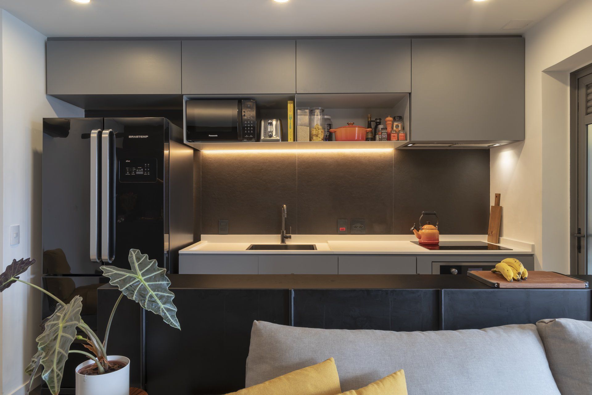 Uma sala de estar com sofá e uma cozinha com geladeira preta