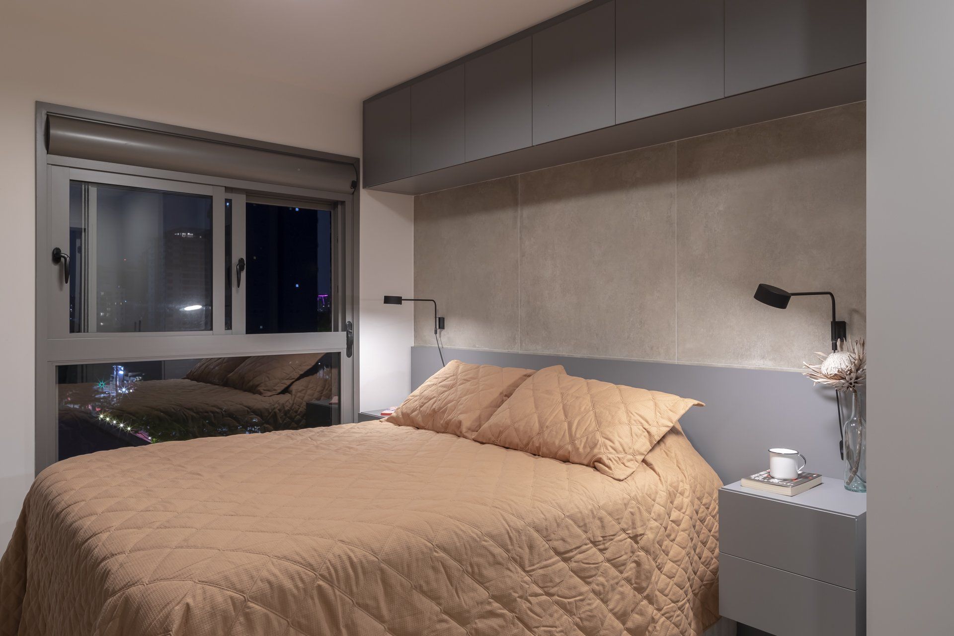 Um quarto com cama, mesa de cabeceira e janela.