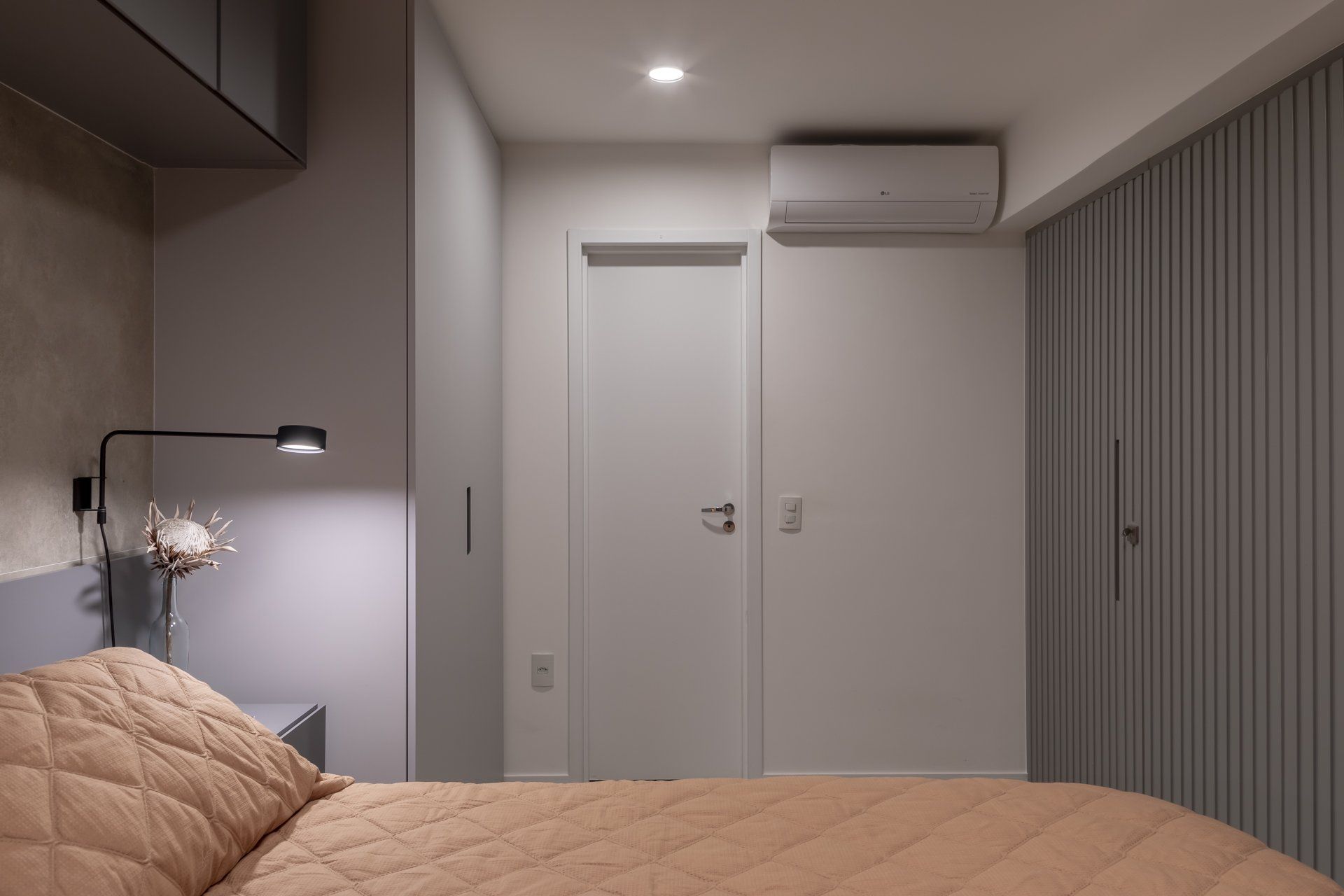 Um quarto com cama, mesa de cabeceira, armários e porta.