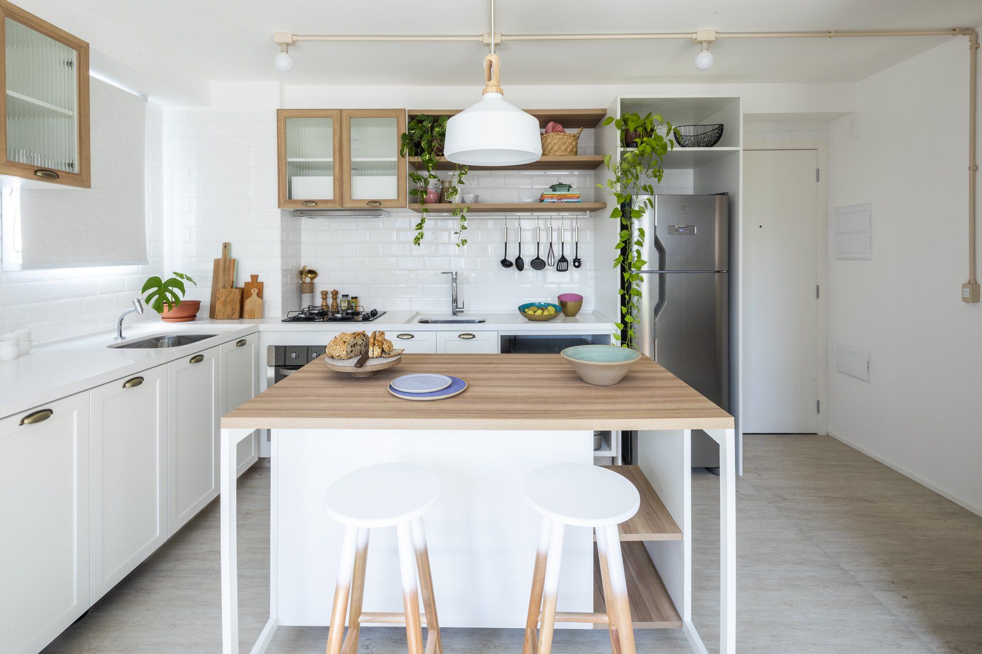 Uma cozinha com armários brancos, mesa e banquetas de madeira.