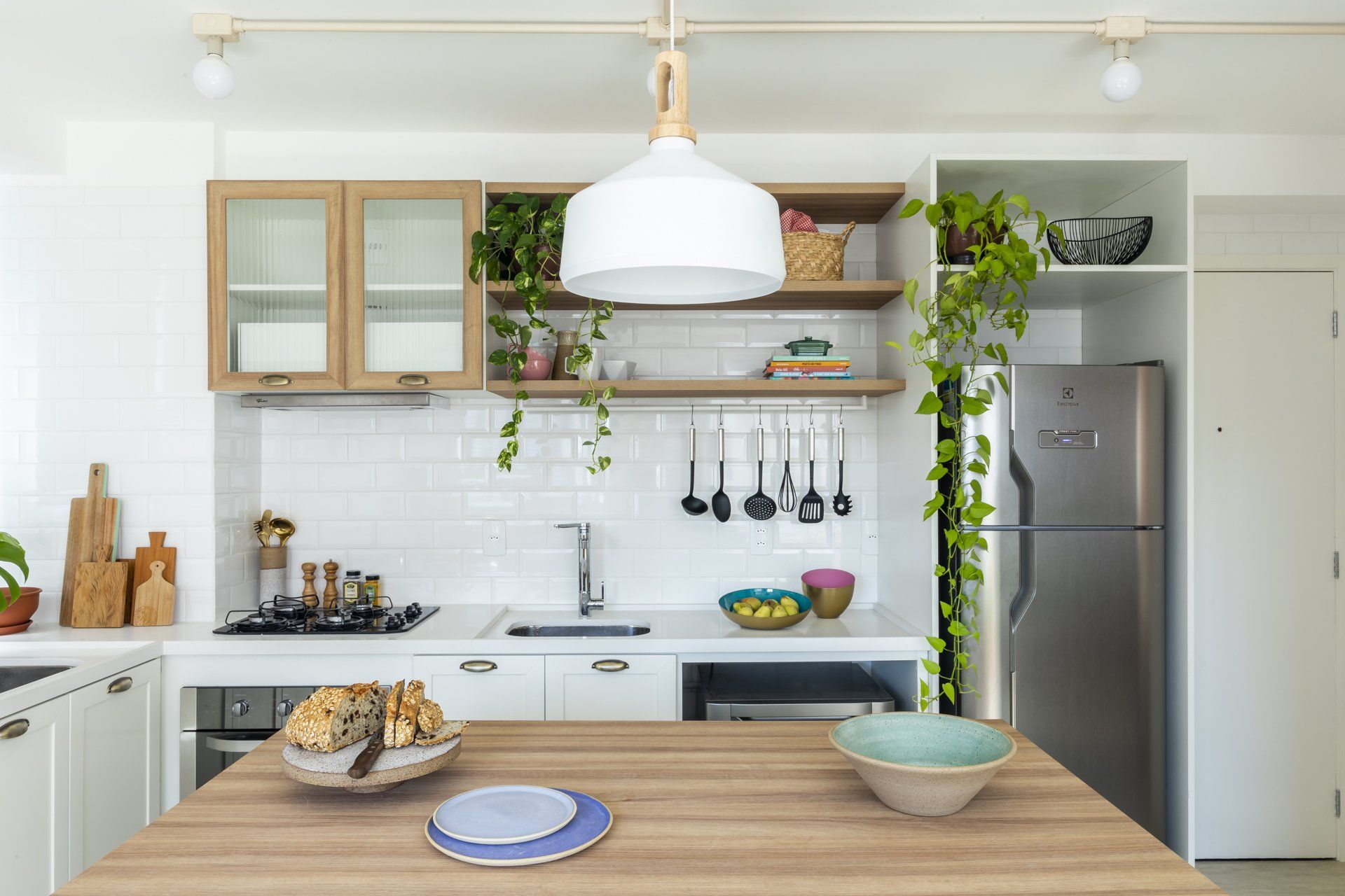 Uma cozinha com armários brancos, geladeira de inox e mesa de madeira.