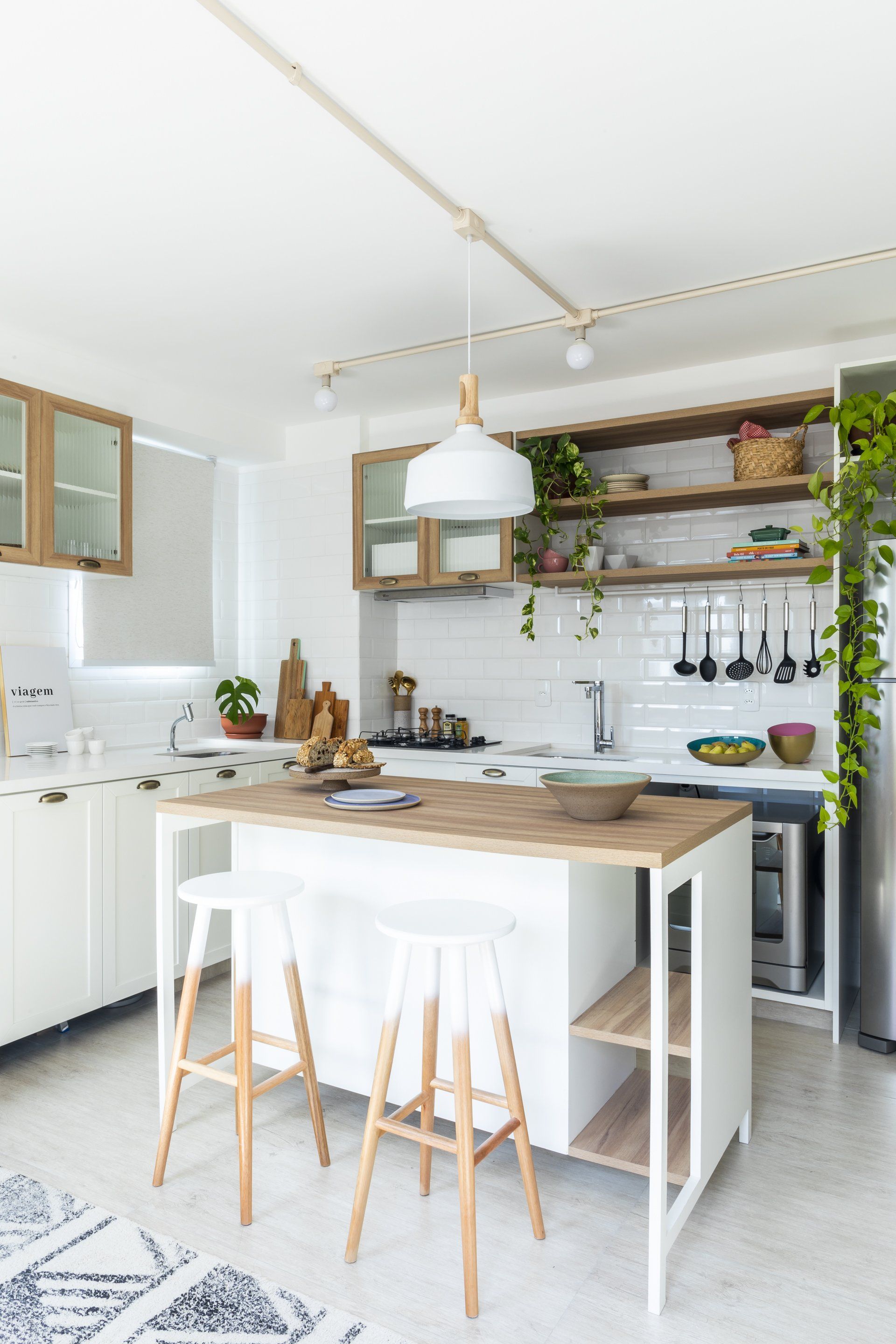 Cozinha com armários brancos, ilha de madeira, banquetas e geladeira.