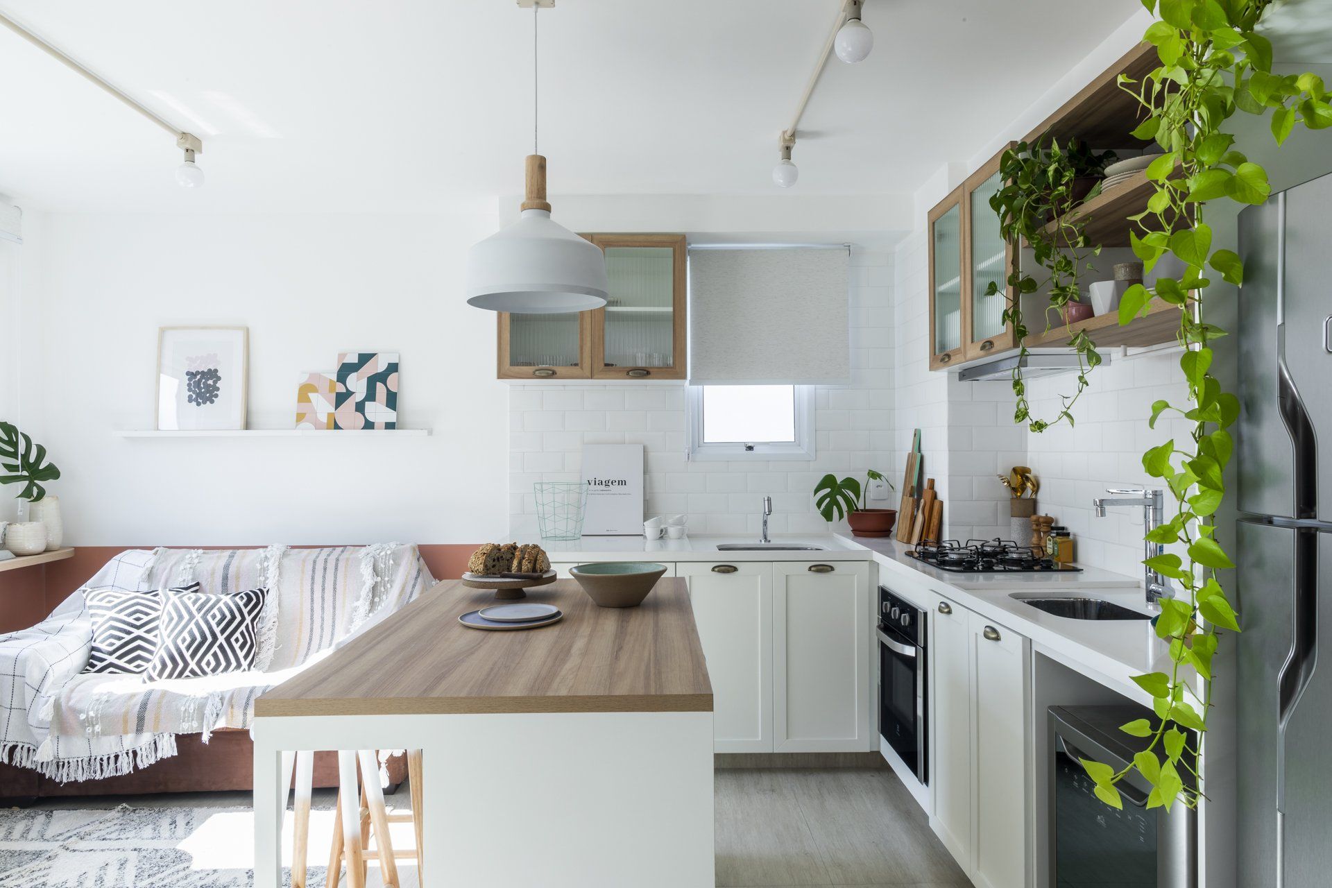 Uma cozinha com armários brancos, mesa de madeira, geladeira e sofá.