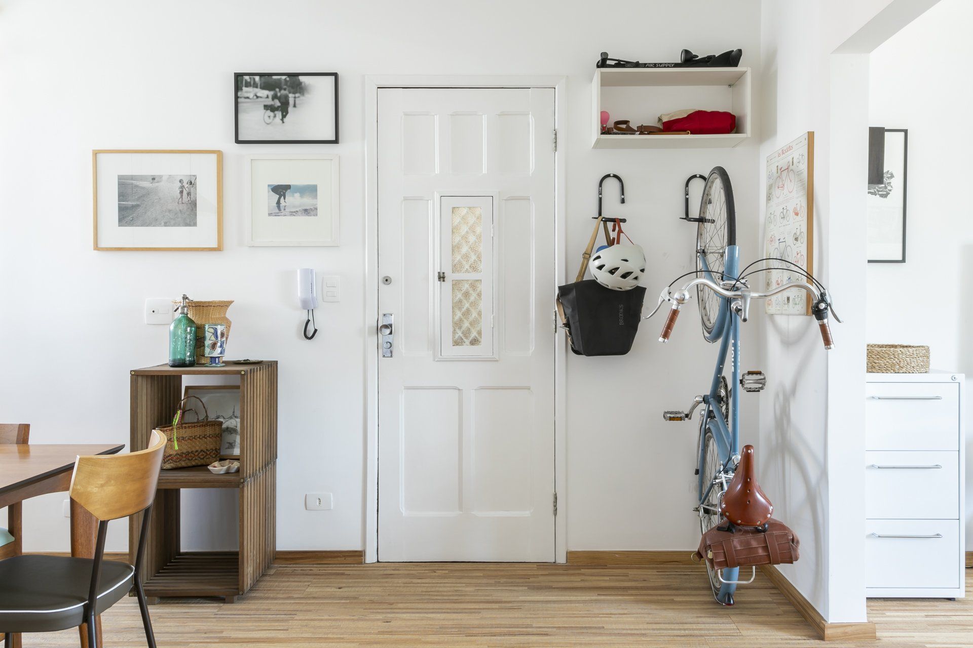 Uma bicicleta está pendurada em um gancho em um corredor ao lado de uma mesa e cadeiras.