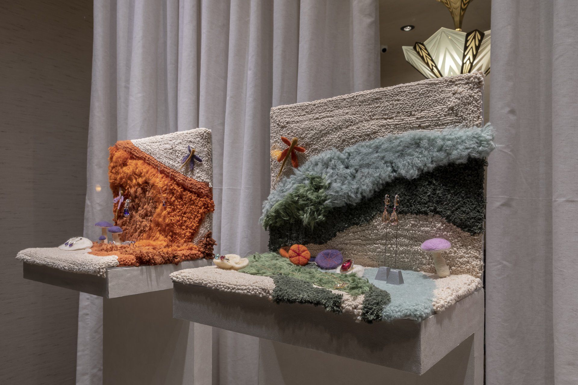 Duas esculturas estão sentadas sobre uma mesa em frente a uma cortina branca.