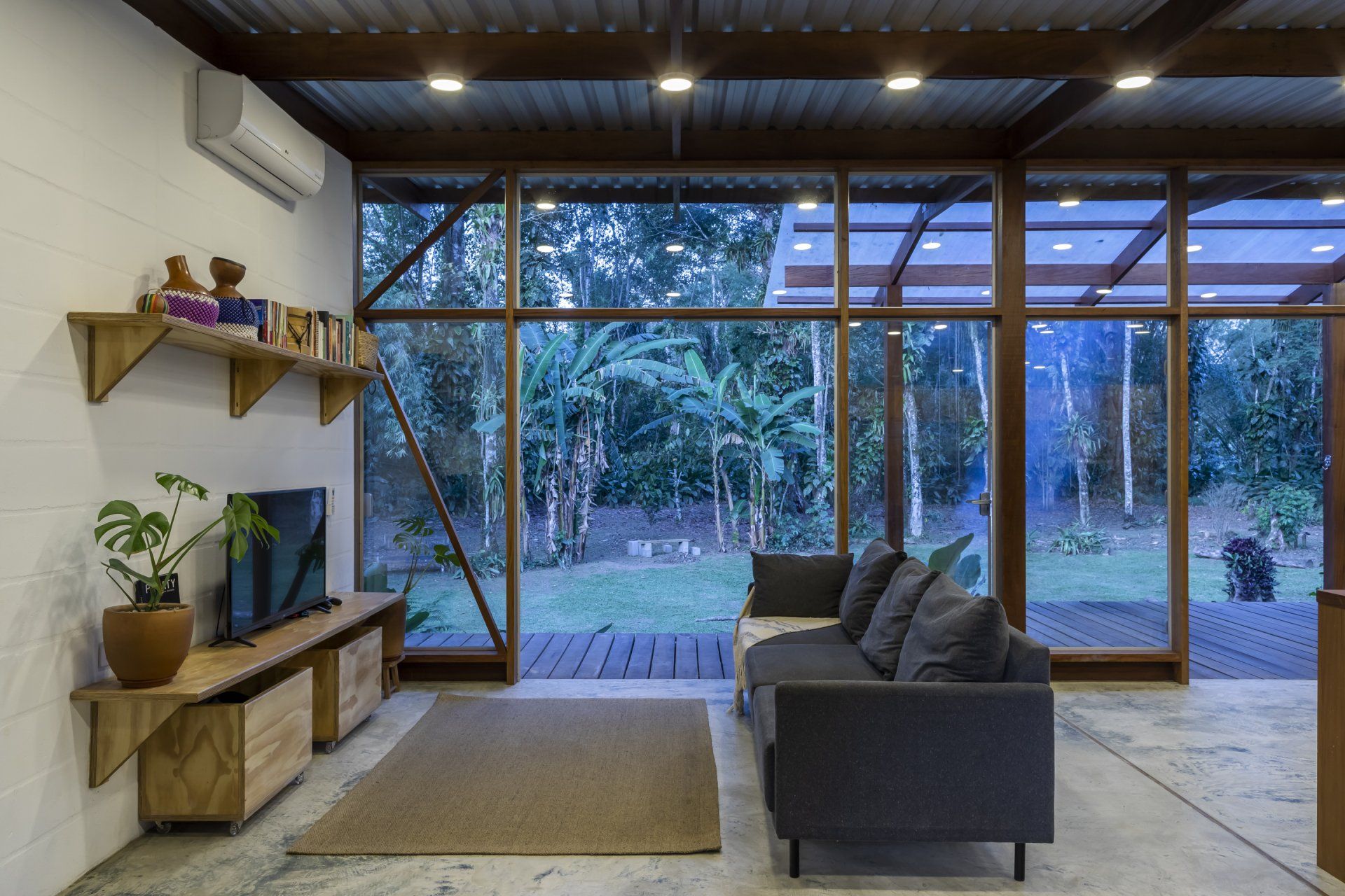 Uma sala de estar com sofá, televisão e muitas janelas.