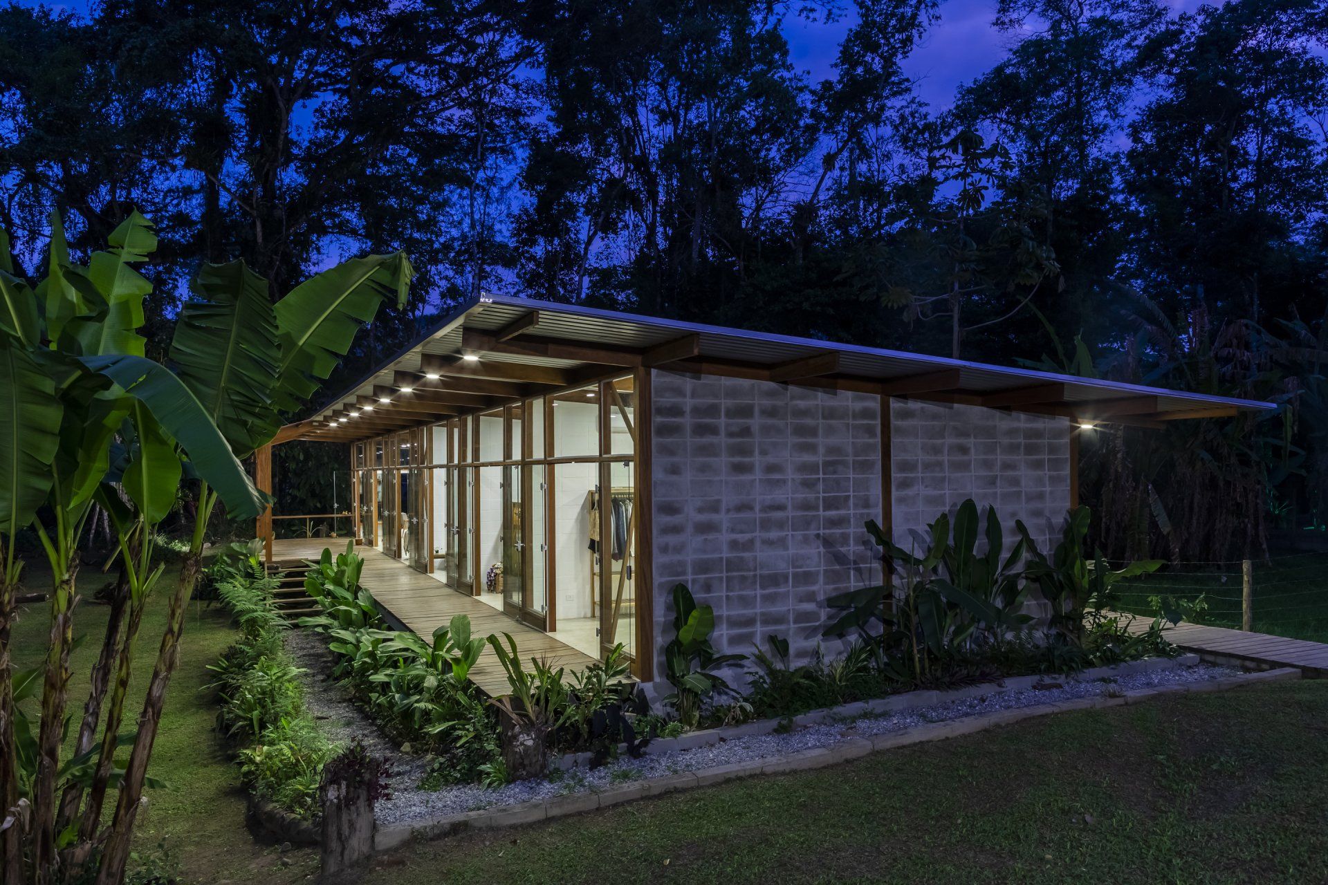 Uma casa com muitas janelas é cercada por árvores à noite.