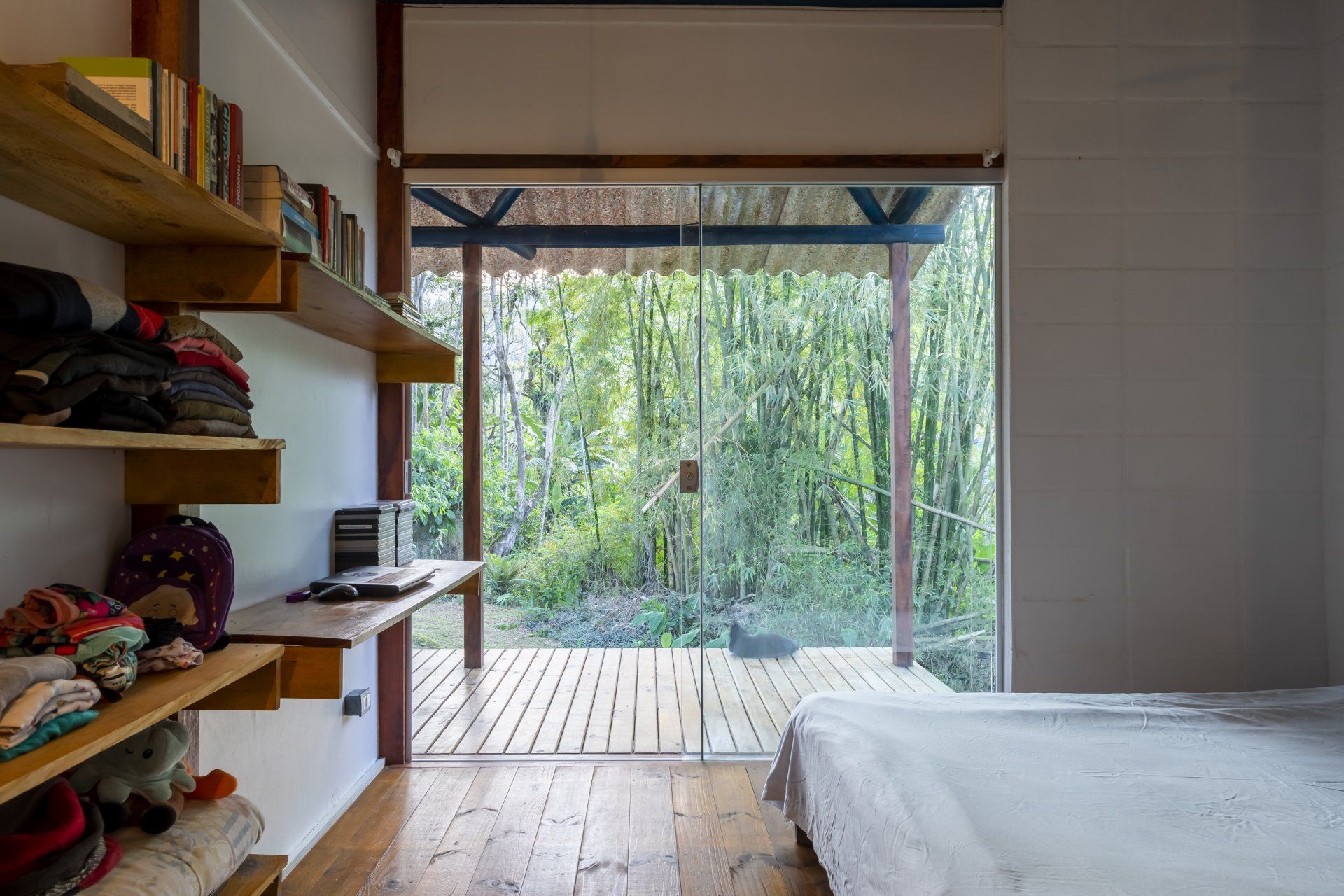 Um quarto com cama, mesa, prateleiras e porta de vidro deslizante.