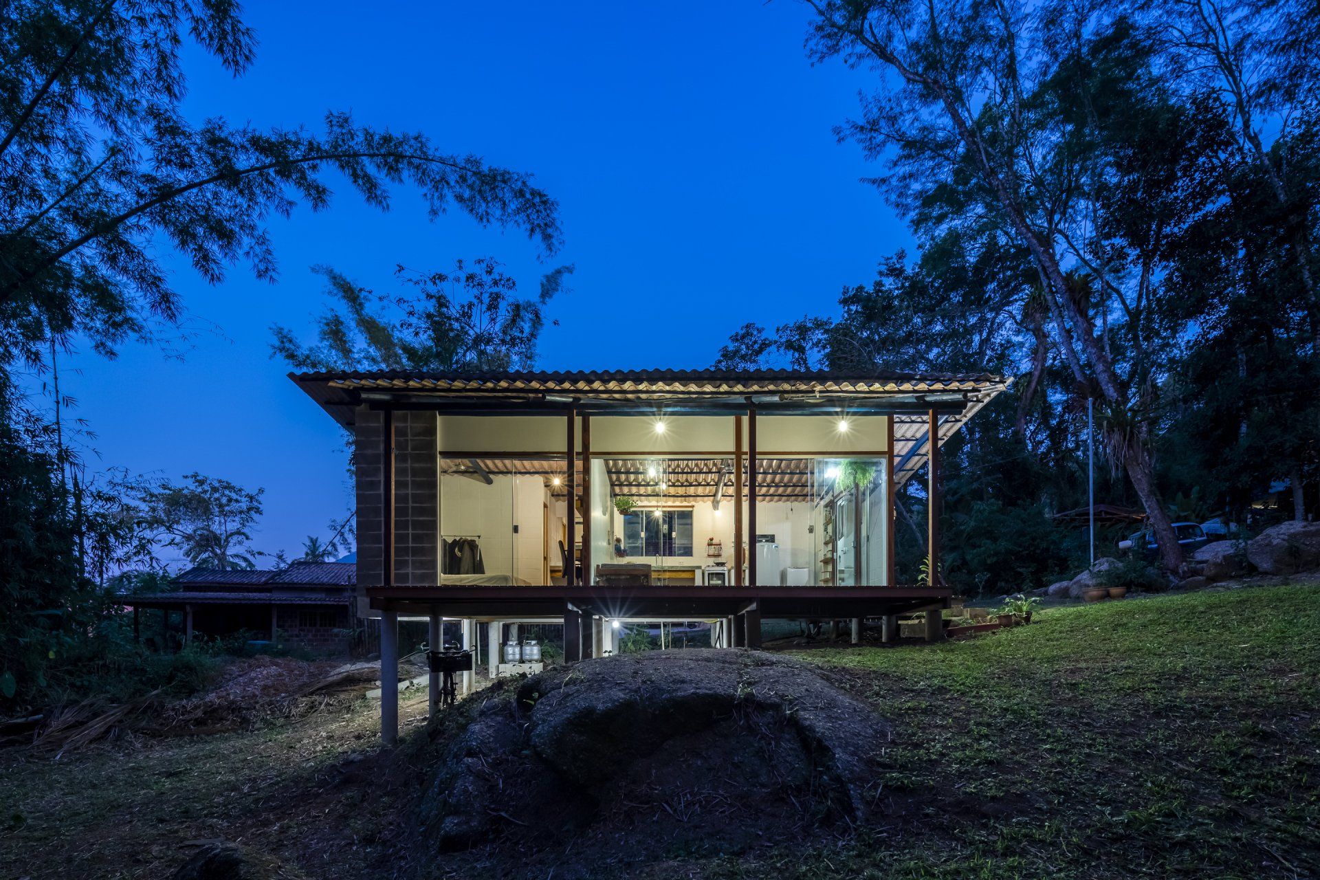 Uma pequena casa com muitas janelas fica iluminada à noite.