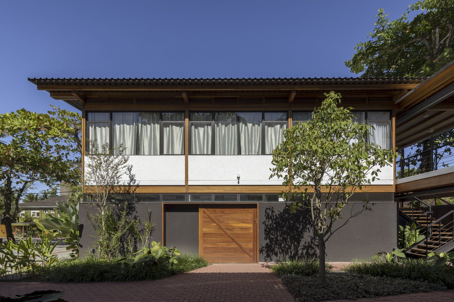 Uma casa grande com porta de madeira e muitas janelas rodeada de árvores.