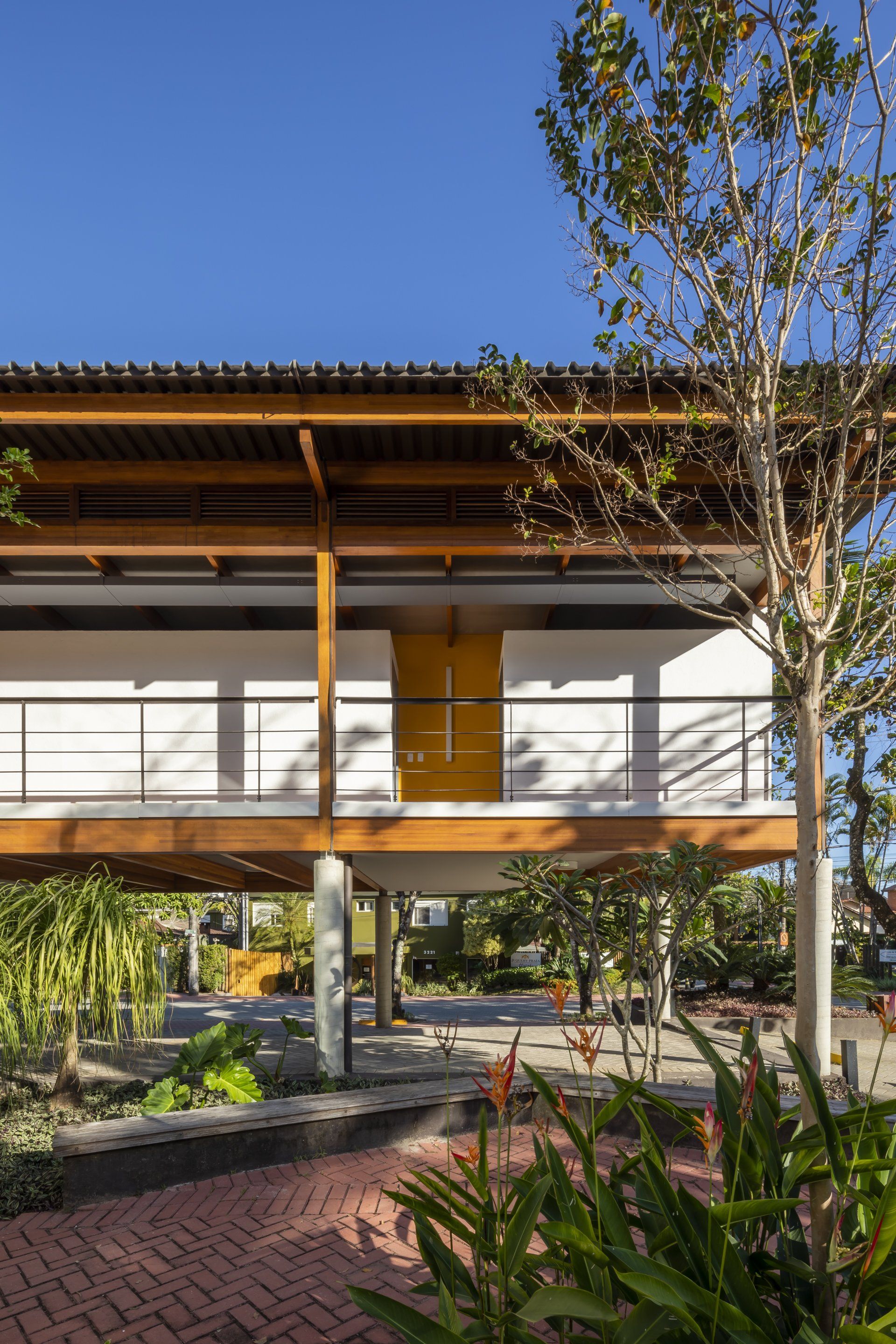 Uma casa com deck de madeira e porta amarela é cercada por árvores.