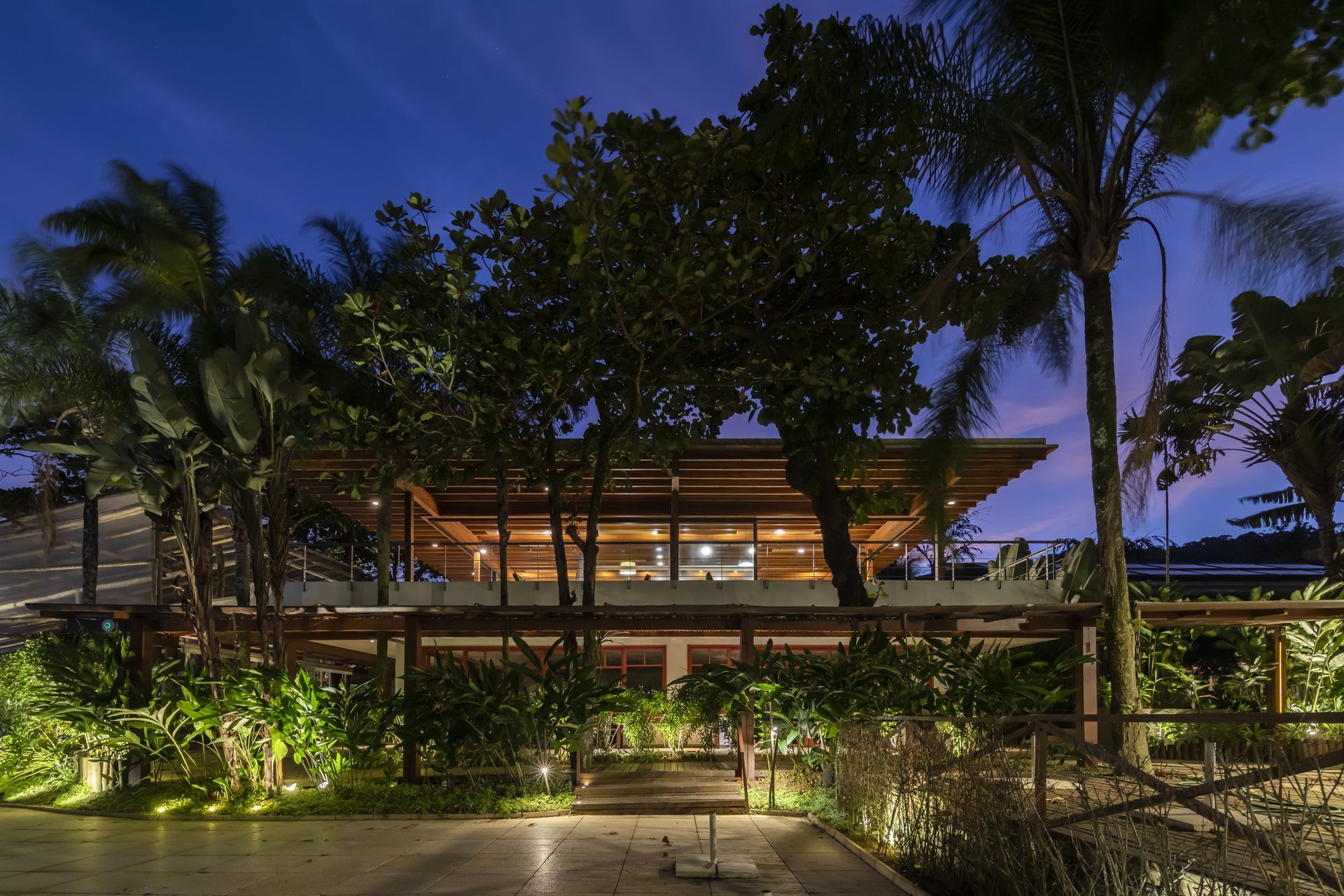 Uma grande casa é cercada por palmeiras à noite.