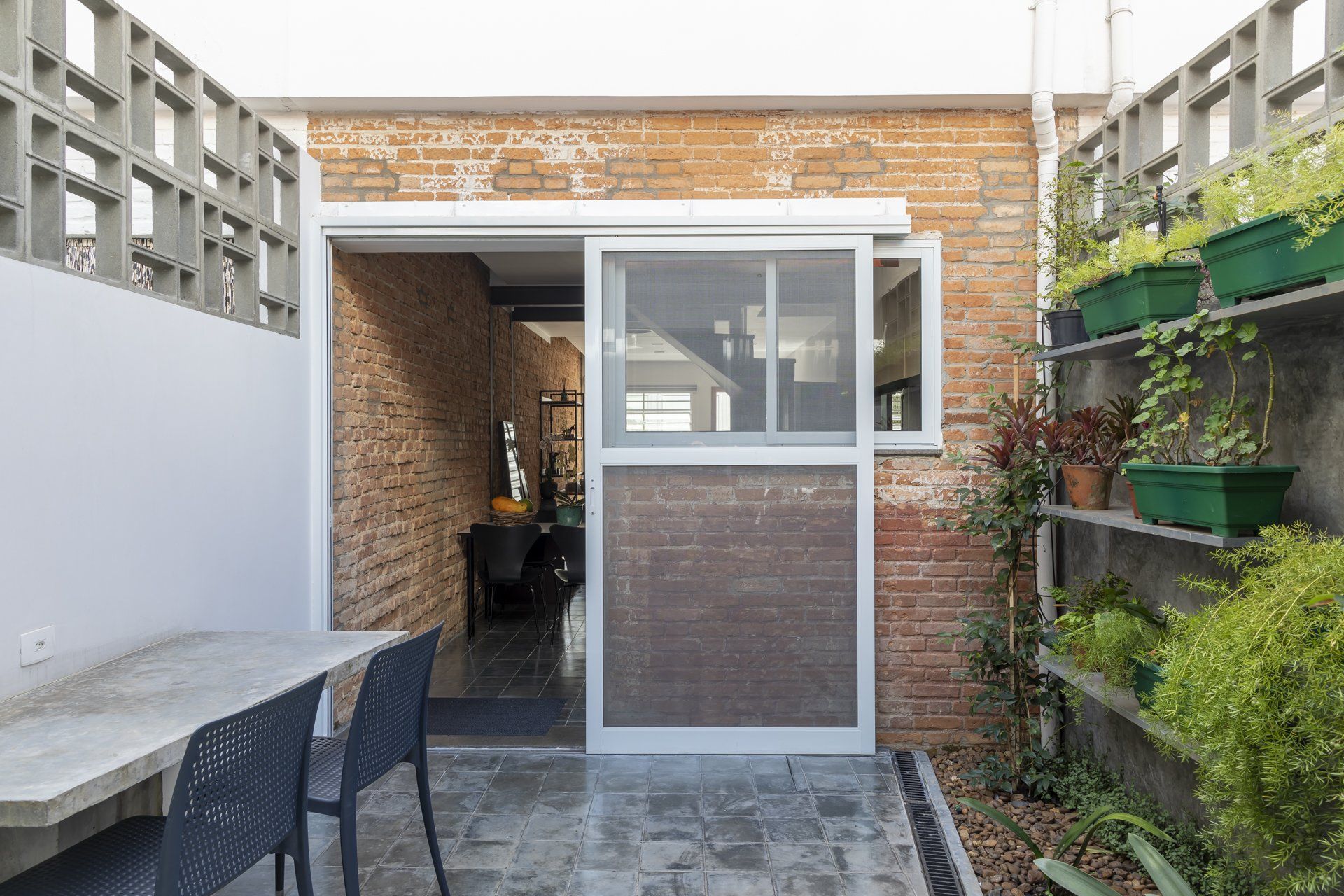 Um prédio de tijolos com uma porta de vidro deslizante e uma mesa e cadeiras na frente.