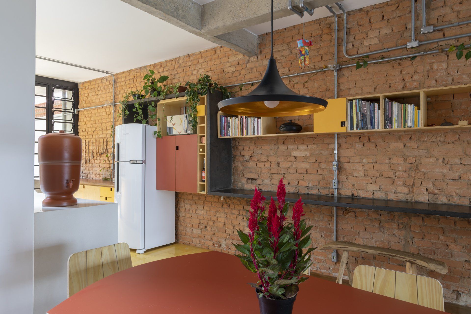 Uma mesa de jantar com um vaso de planta em frente a uma parede de tijolos.